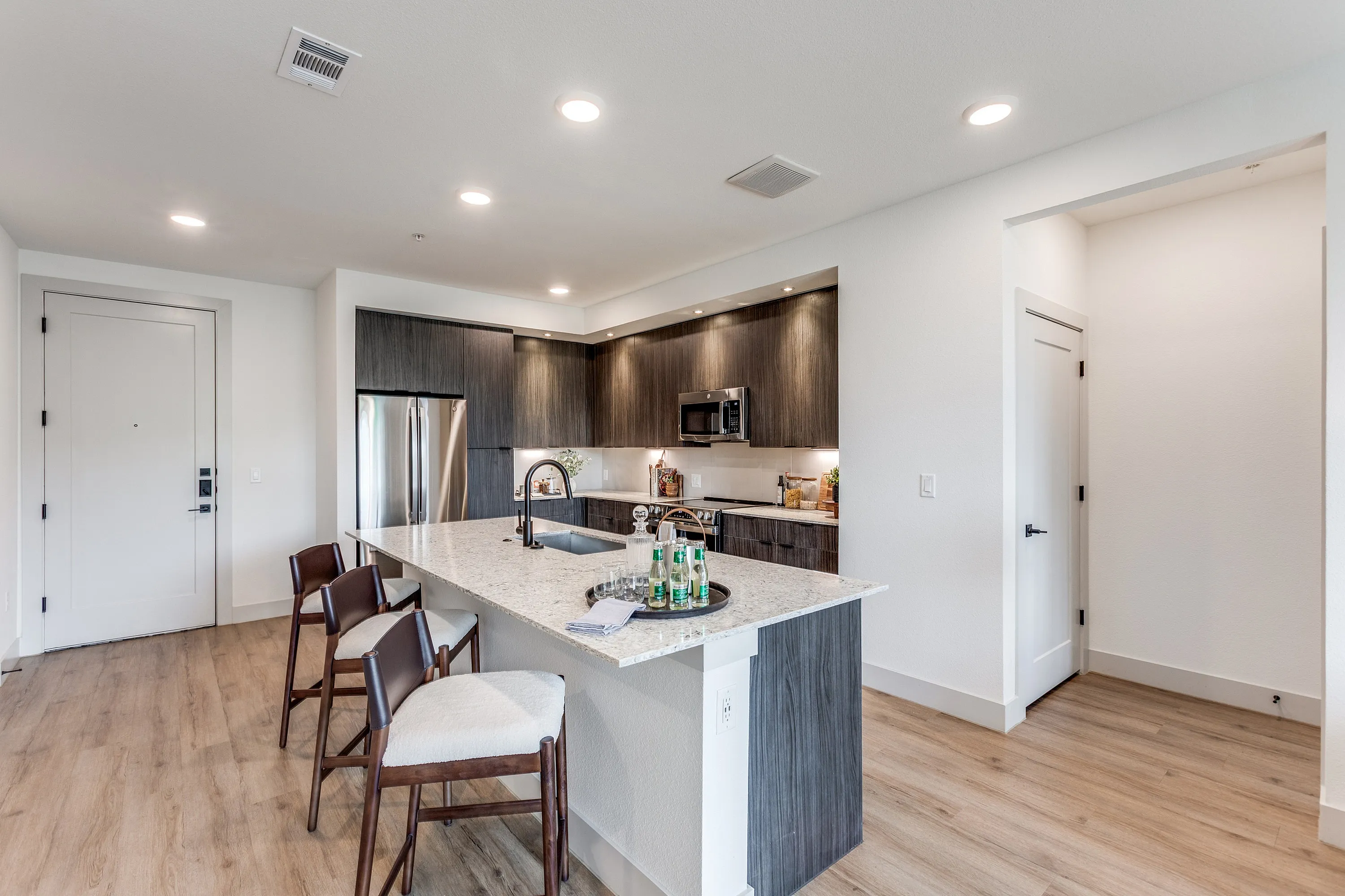 Modern kitchen with a sleek island and seating, stainless steel appliances, and stylish wood cabinetry in a spacious open-plan layout.