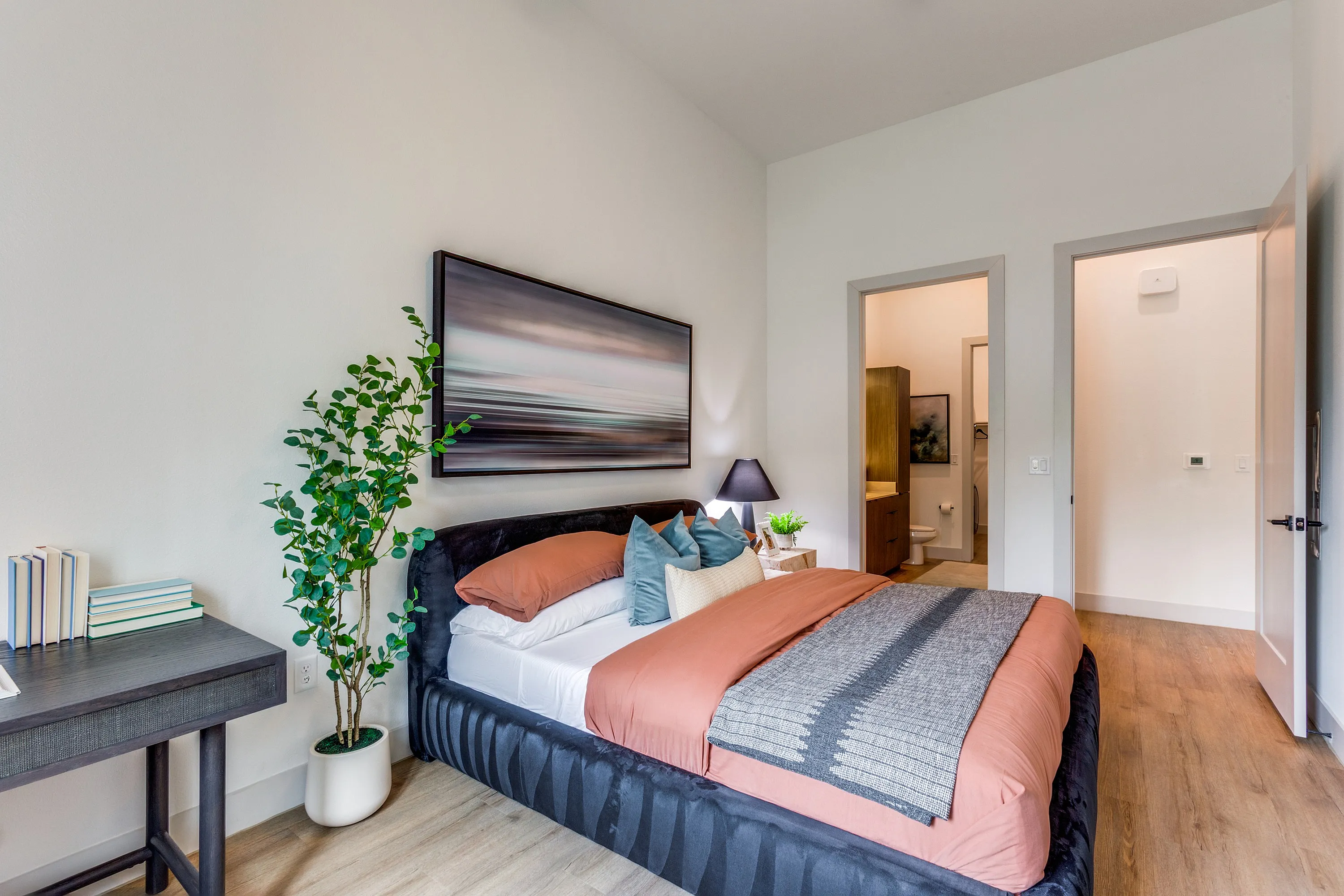 Inviting bedroom with modern decor, featuring a plush bed, cozy pillows, stylish artwork, and warm hardwood flooring.