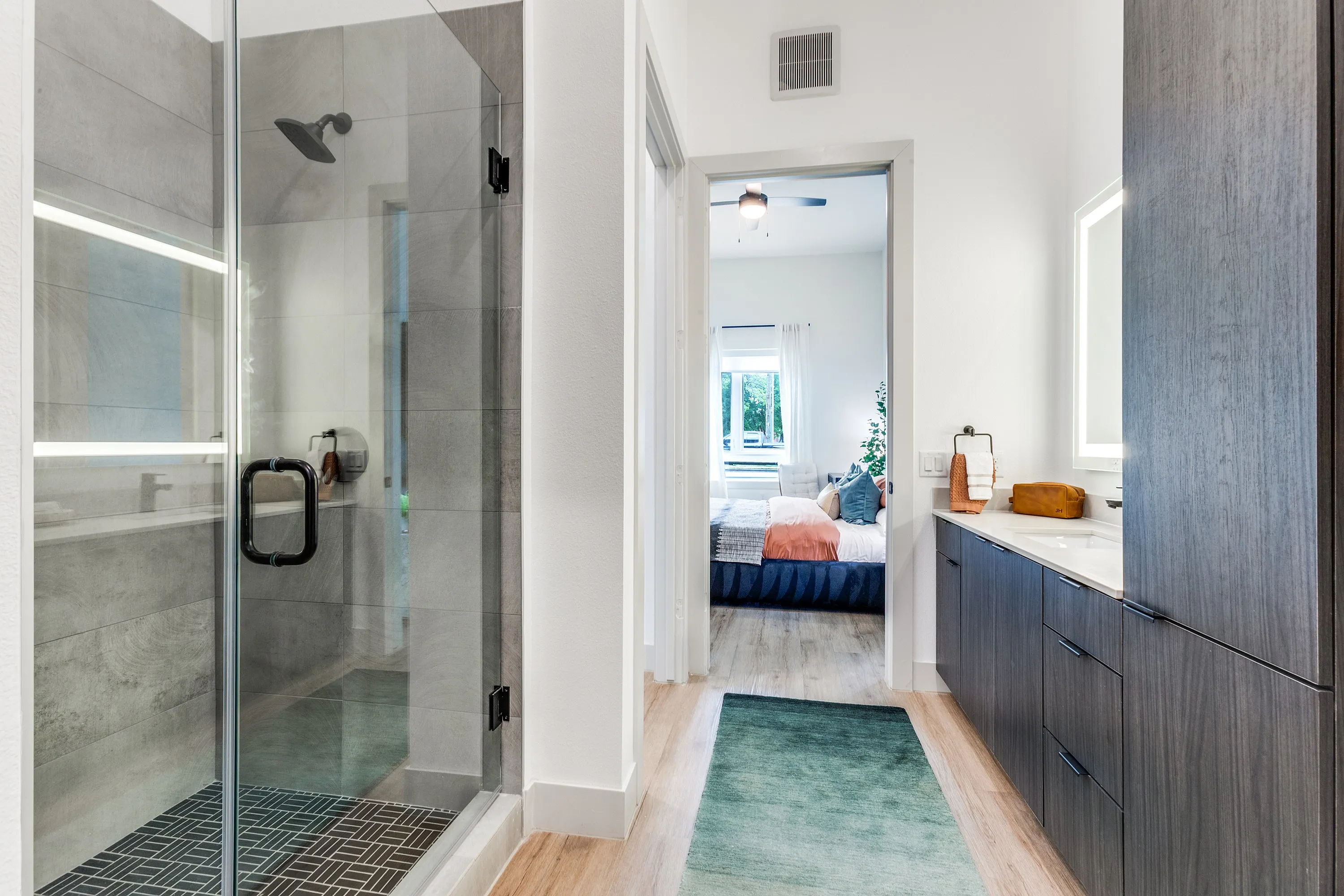 Modern bathroom with sleek glass shower enclosure leading to a cozy bedroom featuring natural light and chic decor.