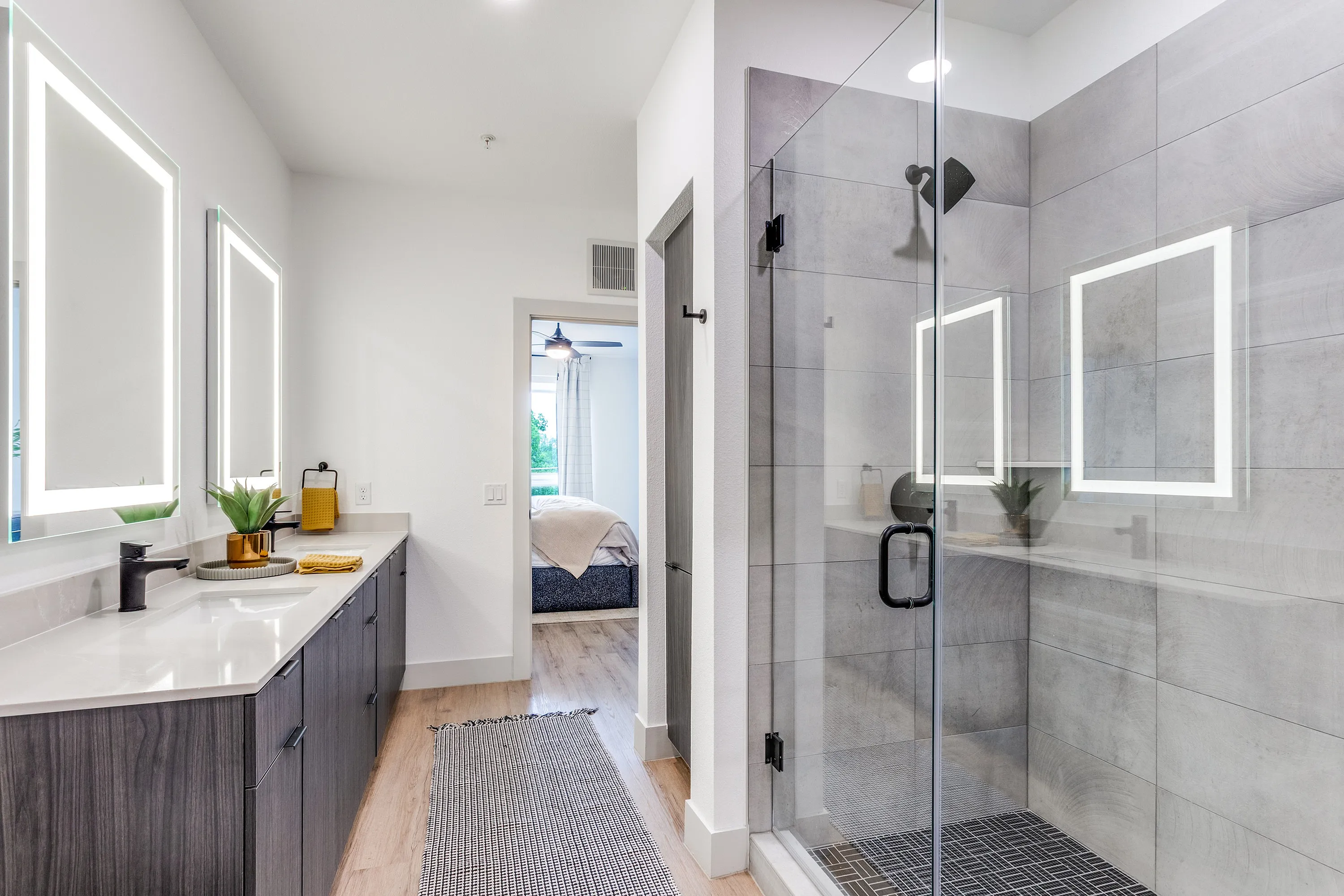 Sleek modern bathroom with illuminated mirrors, glass-enclosed shower, and direct access to a cozy bedroom.
