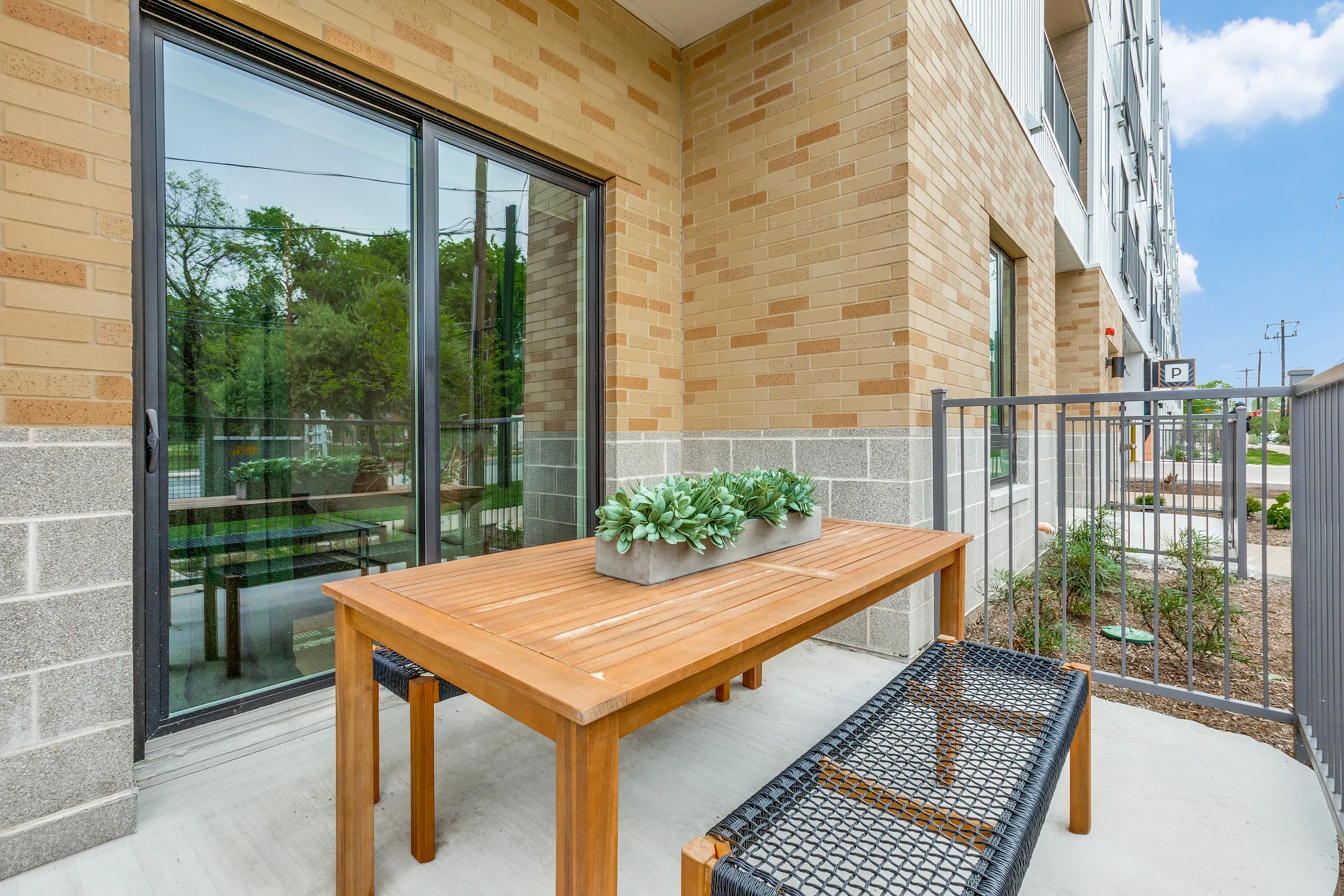 Charming apartment patio with a sleek wooden table, stylish outdoor seating, and lush potted plants, perfect for relaxing under the sun.