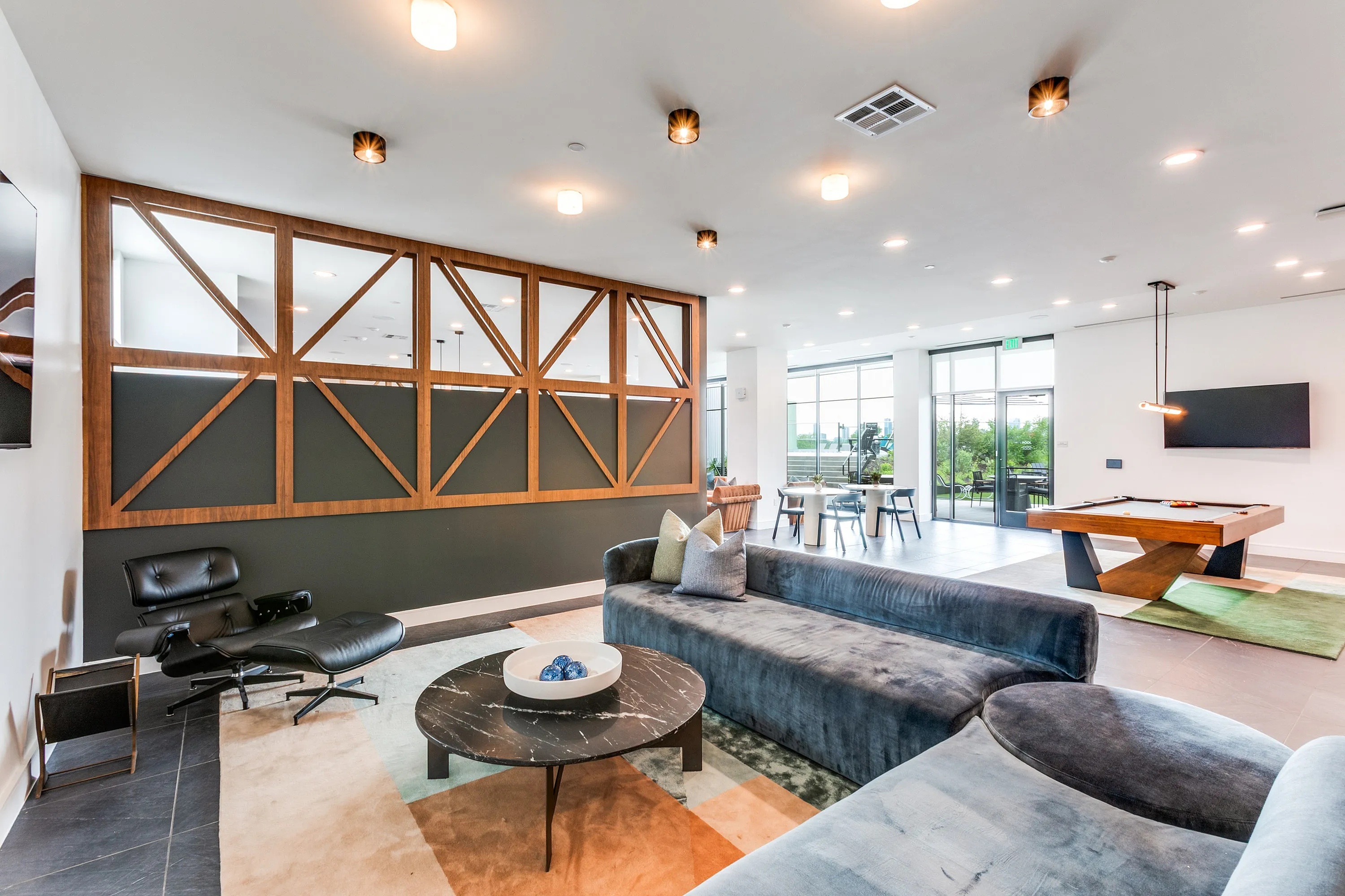 Luxurious lounge space with modern decor, plush seating, sleek pool table, and floor-to-ceiling windows opening to a vibrant outdoor view.