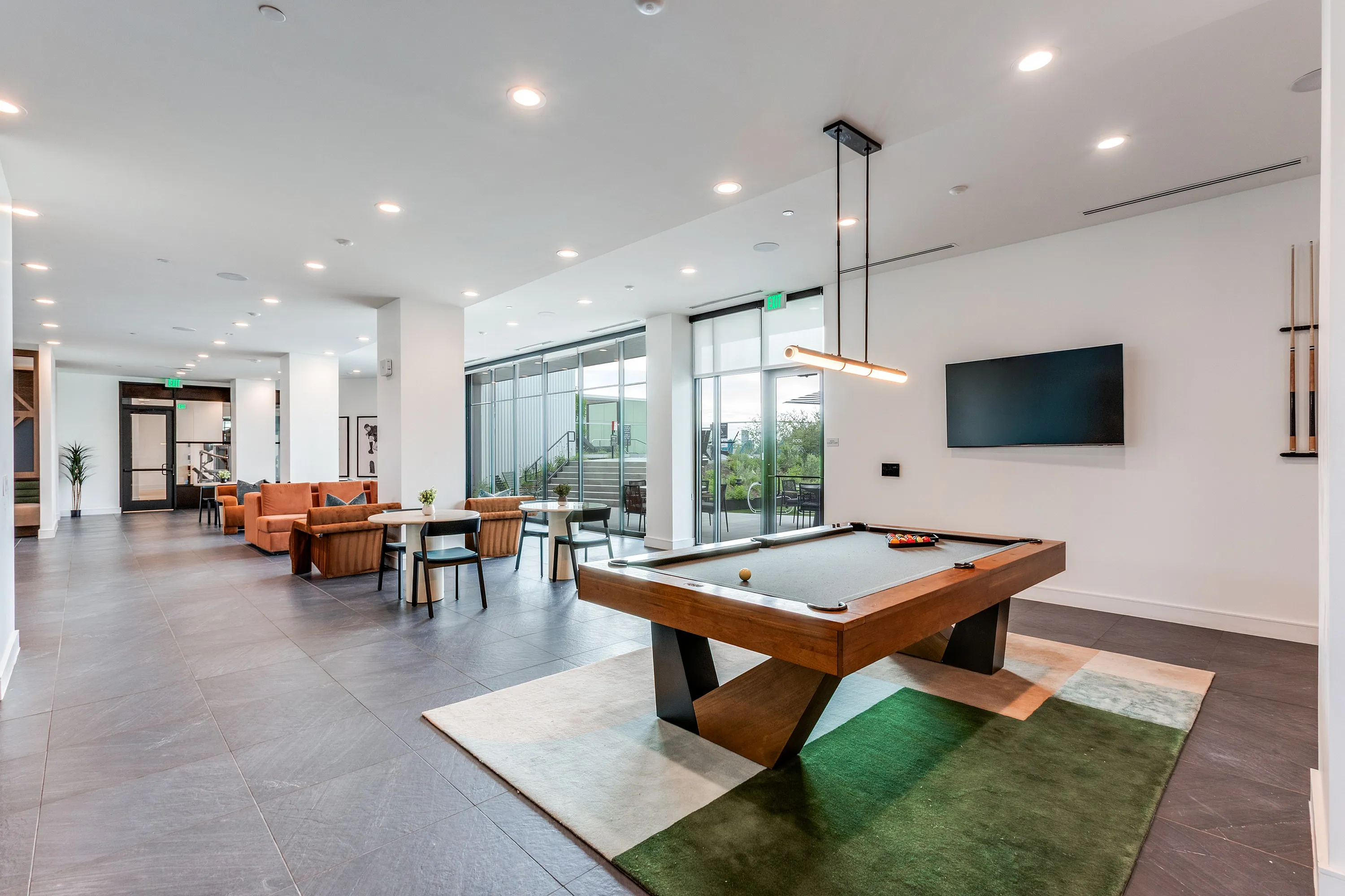 Modern recreational lounge featuring a sleek pool table, cozy seating with orange sofas, and a spacious dining area under soft lighting.