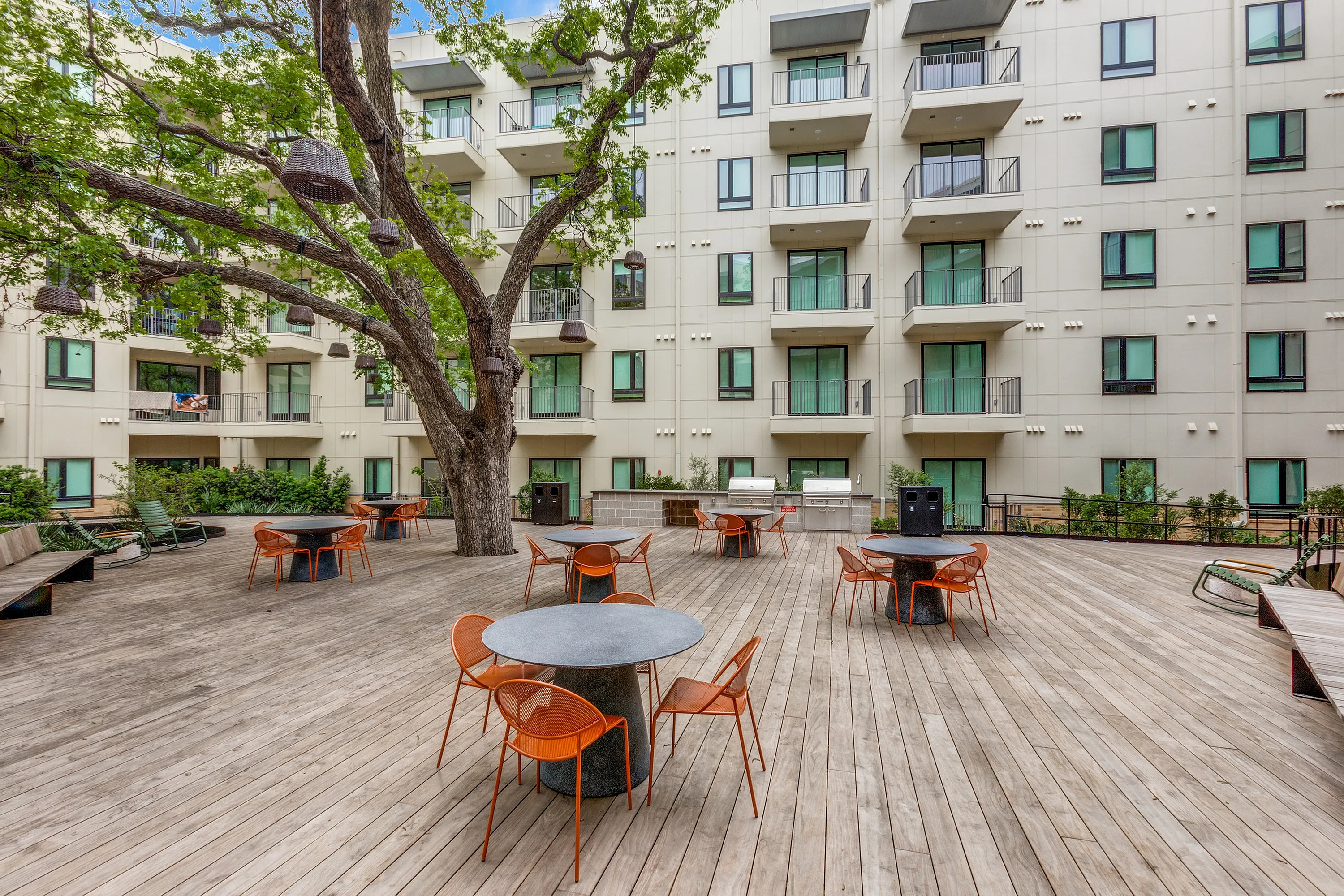 Modern apartment courtyard with stylish outdoor seating, lush greenery, and inviting communal areas under a shady tree.