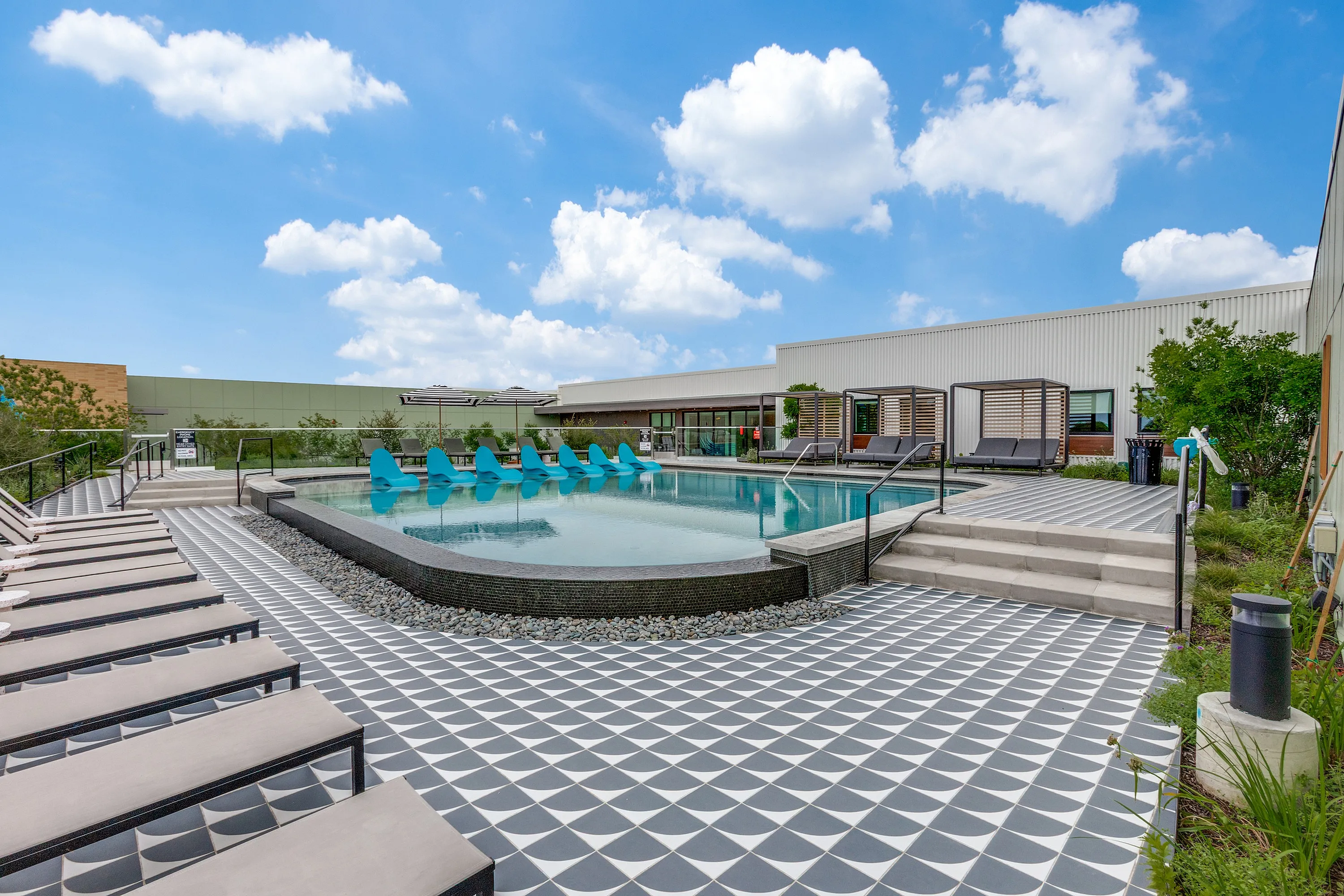 Luxurious outdoor pool area with stylish lounge chairs and private cabanas under a bright blue sky.