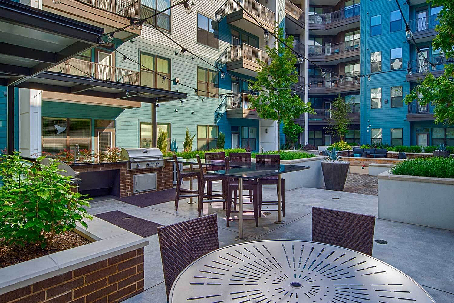 Chic apartment courtyard featuring a modern outdoor kitchen, stylish seating area, and lush greenery.