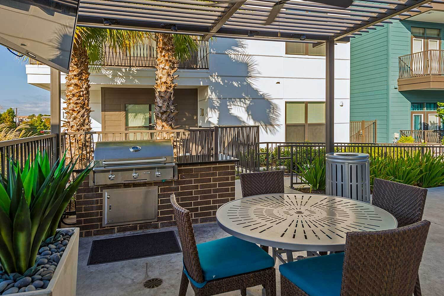 Charming outdoor patio with modern grill, stylish dining set, and lush greenery in a welcoming apartment complex.