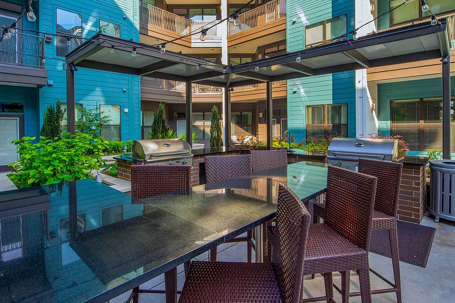 Chic apartment courtyard featuring modern grills, elegant seating, and lush greenery under a stylish pergola.