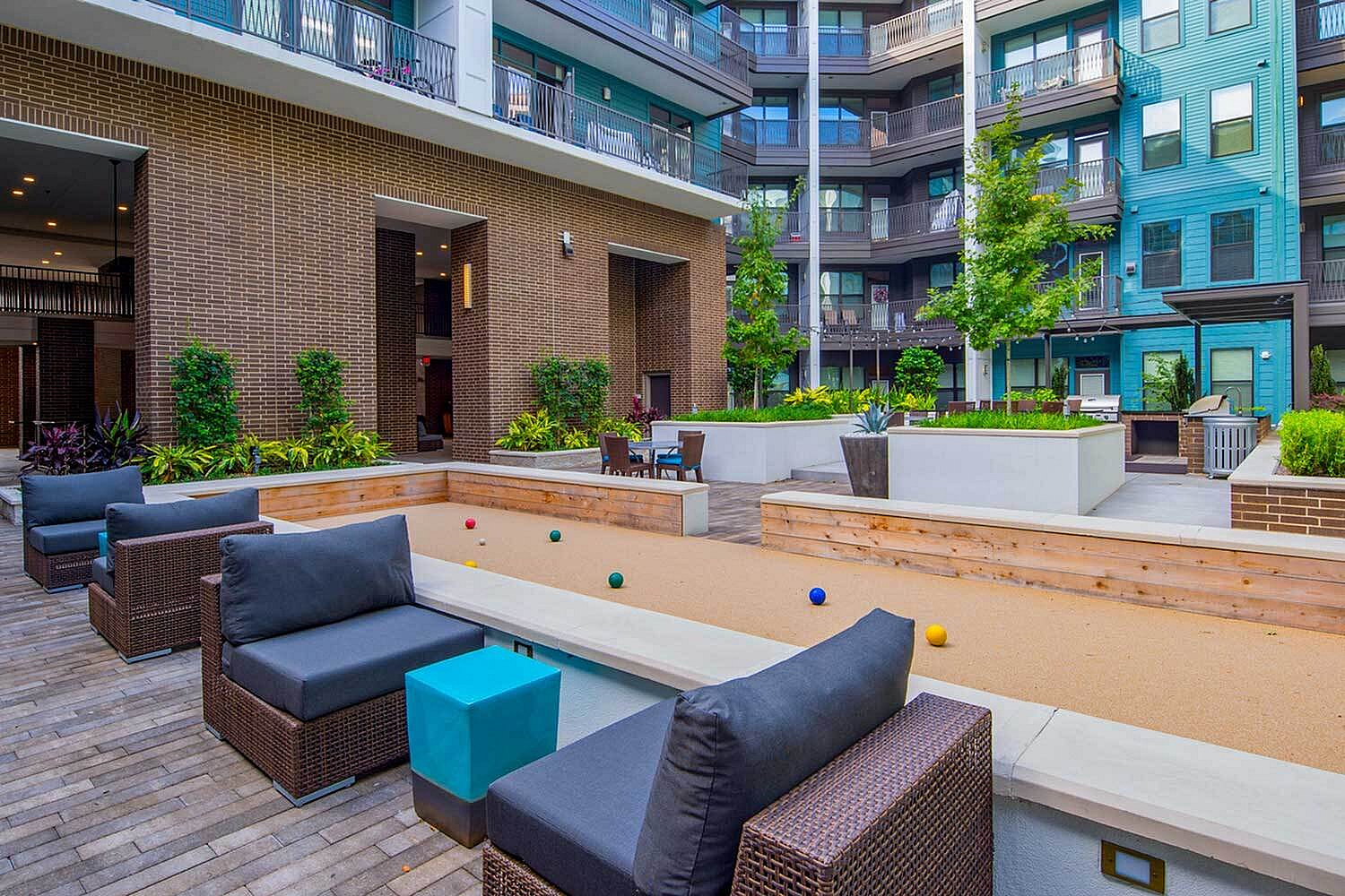 Vibrant courtyard with modern seating, lush greenery, and bocce ball area at a stylish apartment complex.