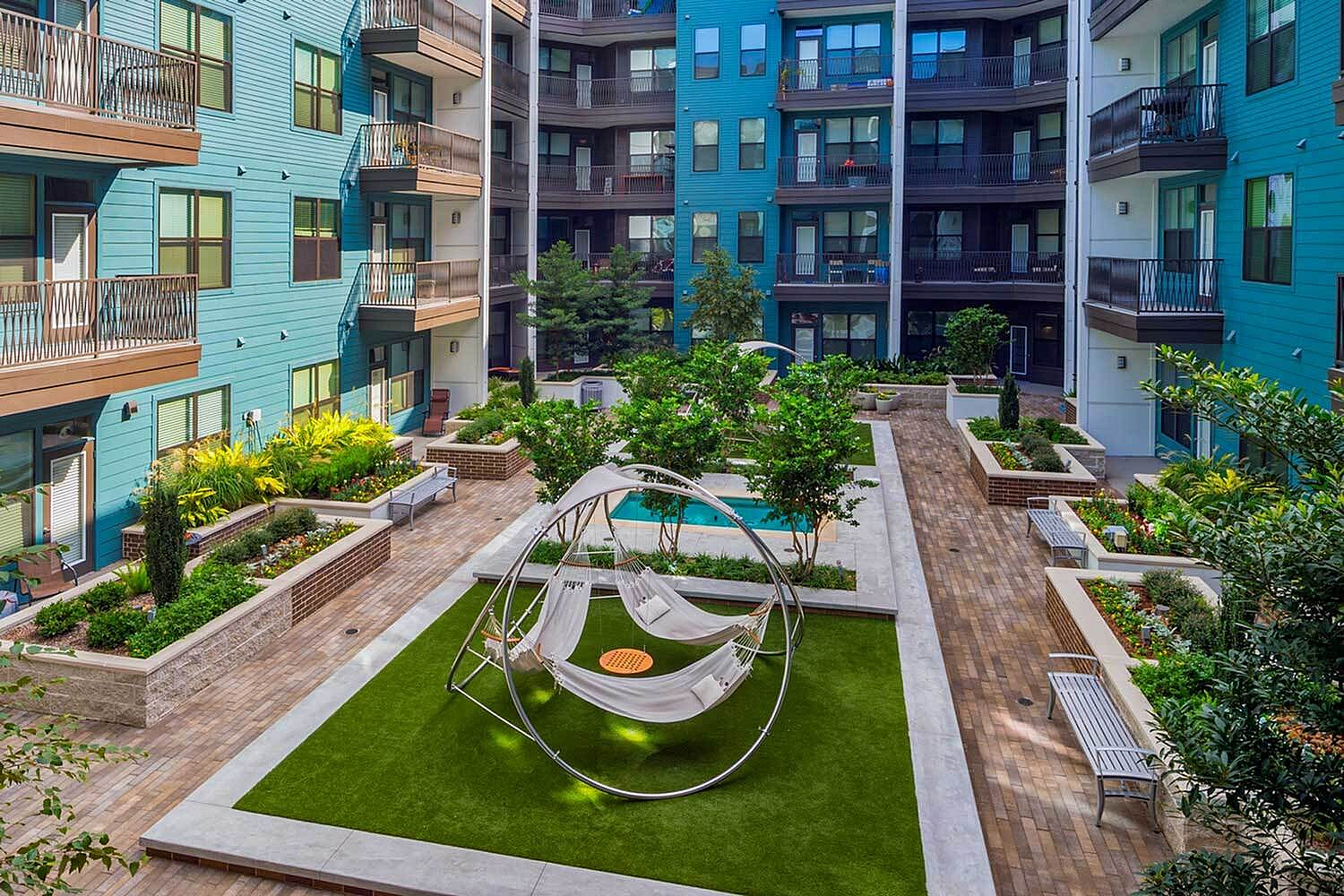 Vibrant apartment courtyard featuring lush greenery, elegant seating, and a modern hammock area offering a tranquil escape.