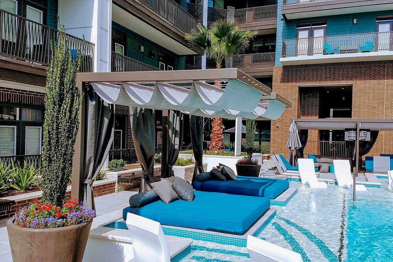 Luxurious poolside oasis with stylish cabanas, vibrant blue sun loungers, and lush greenery in a modern apartment complex.
