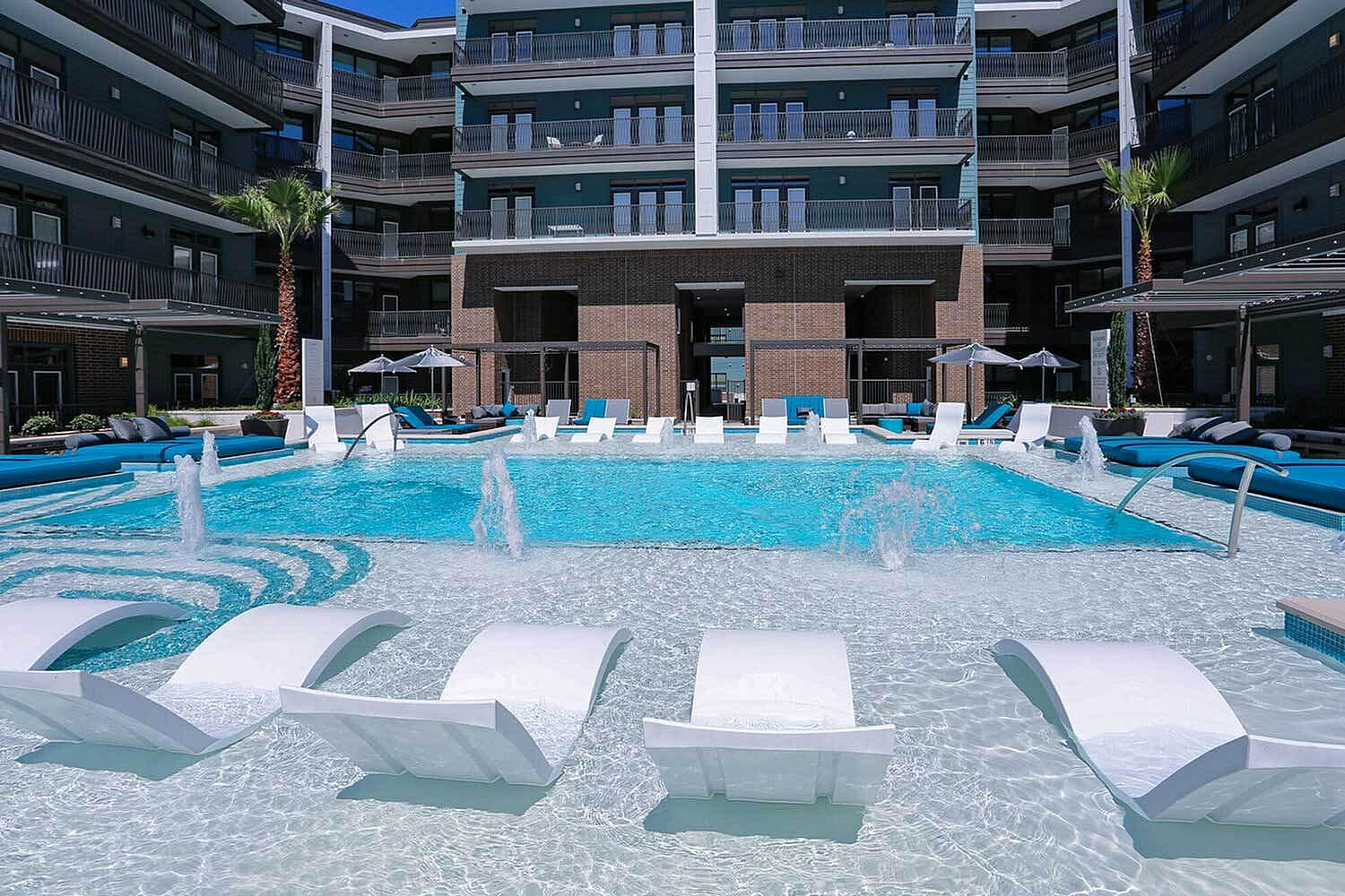 Luxurious apartment complex with a sparkling pool, stylish lounge chairs, and elegant palm trees for a resort-style living experience.
