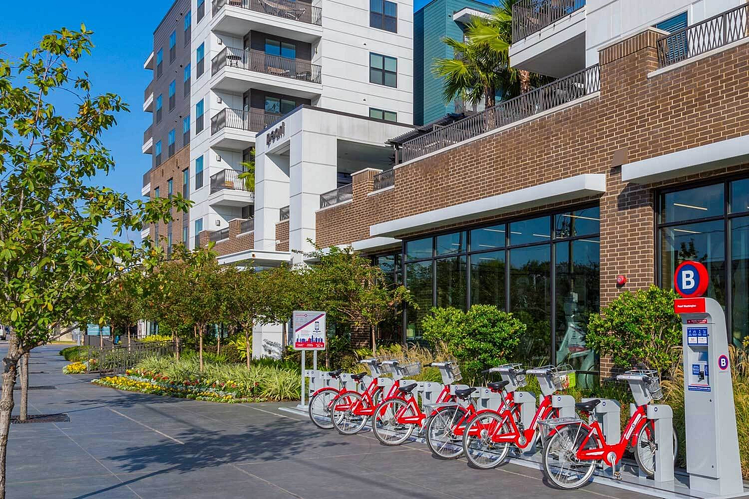 Vibrant urban apartment complex with modern architecture, lush greenery, and convenient bike-sharing station.