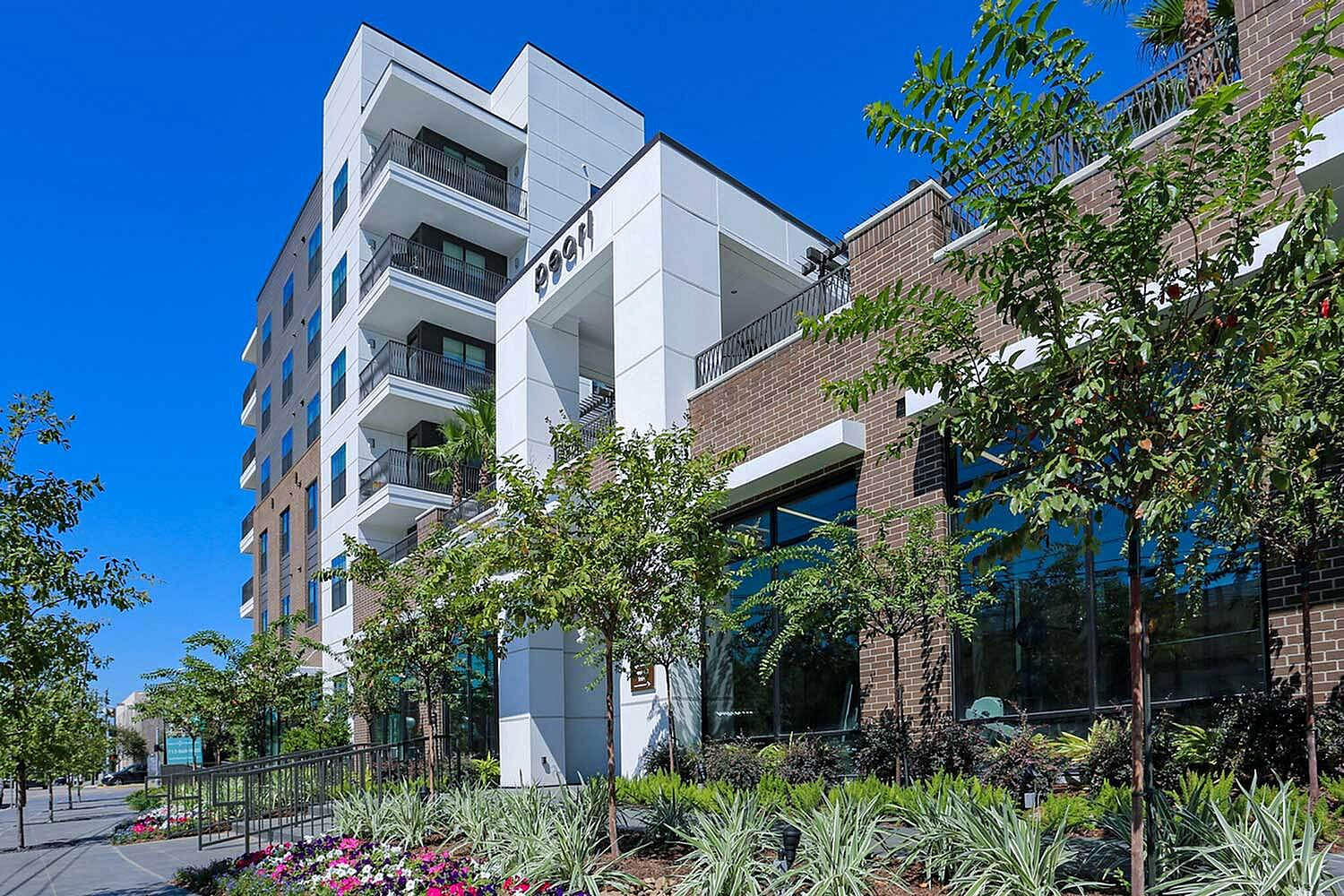Contemporary apartment building with balconies and lush landscaping under a clear blue sky.