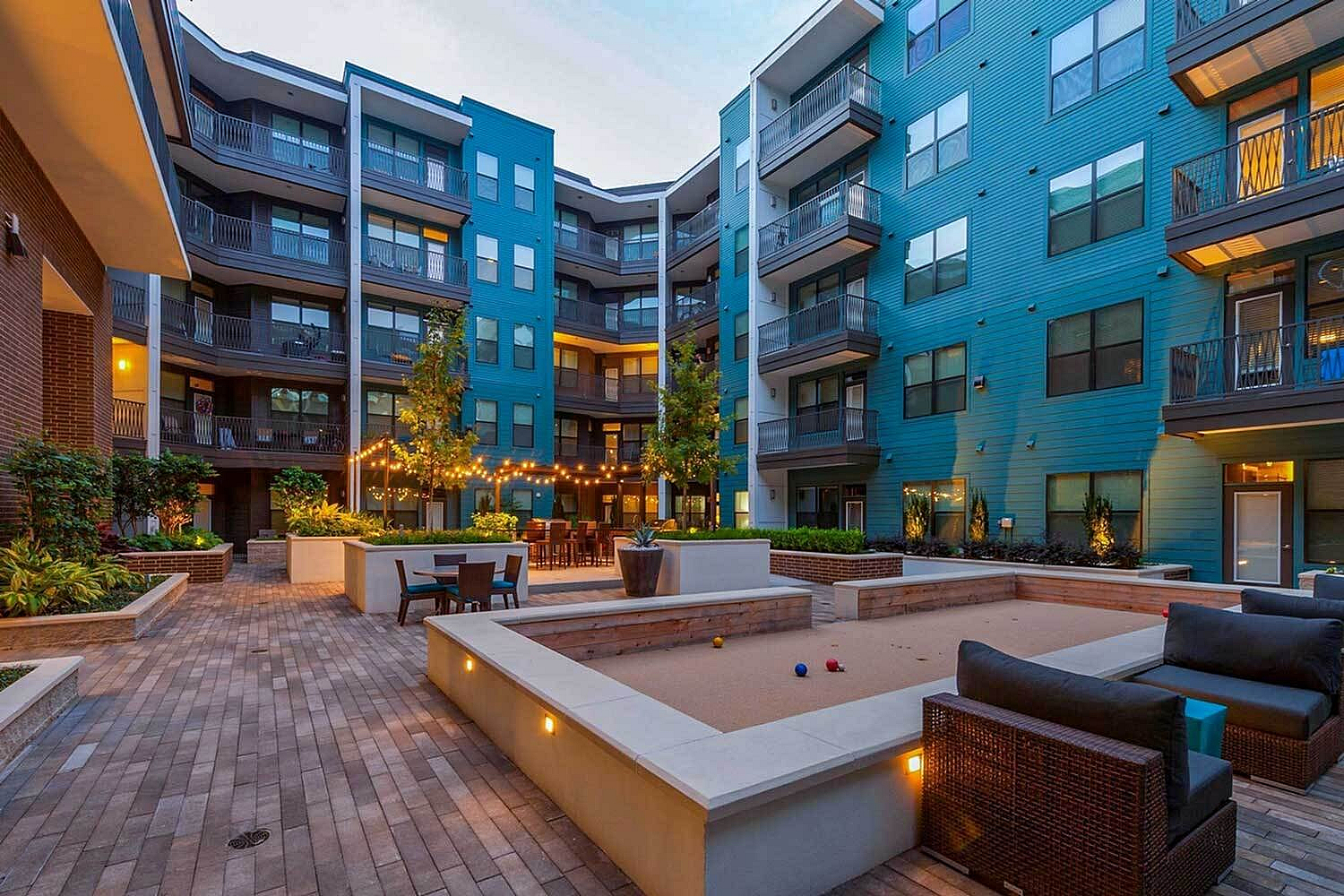 Chic apartment courtyard featuring modern seating, vibrant greenery, and ambient string lighting for an inviting atmosphere.