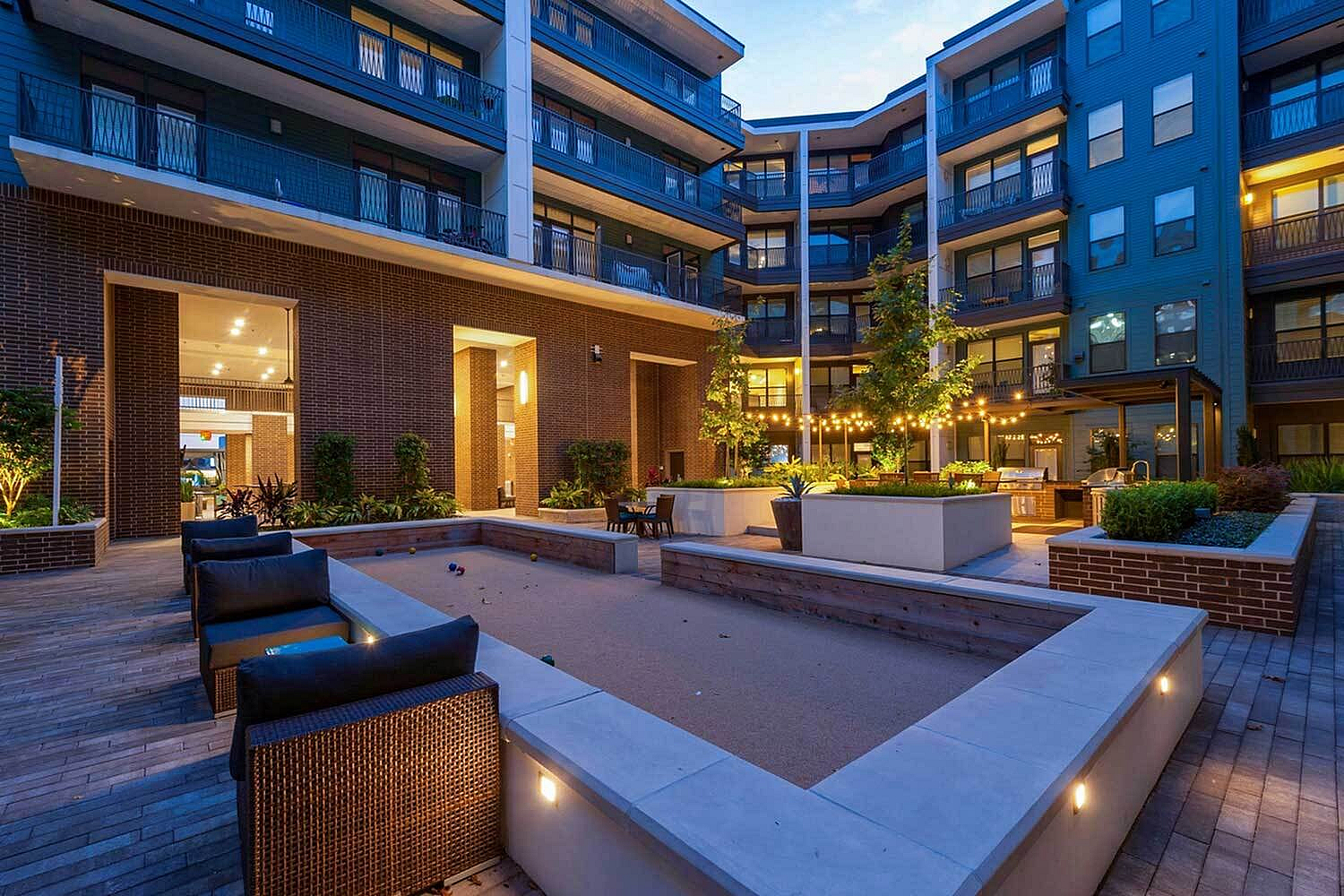 Chic urban courtyard in modern apartment complex adorned with ambient string lights, lush greenery, and comfortable seating areas.