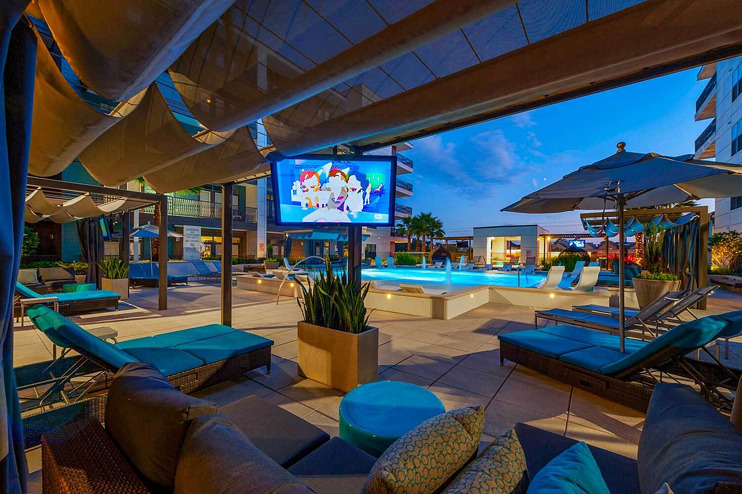 Luxurious poolside lounge area with modern cabanas and large screen TV, perfect for relaxation and entertainment.