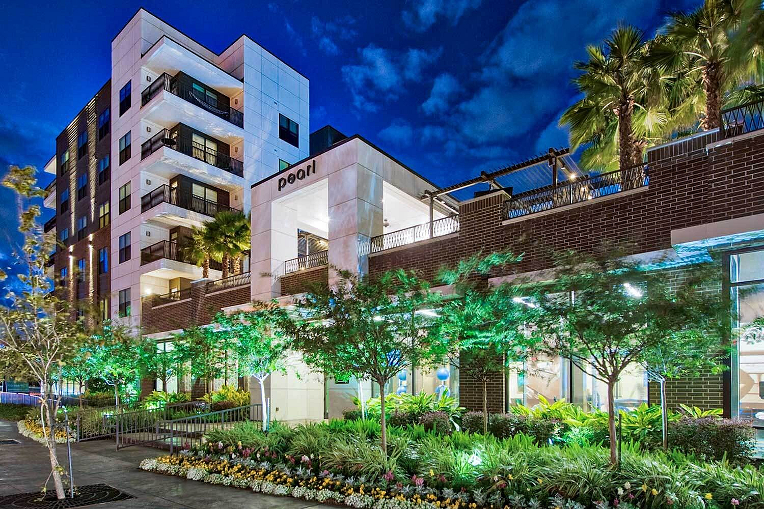 Elegant apartment complex at night, showcasing modern architecture with lush landscaping and ambient lighting.