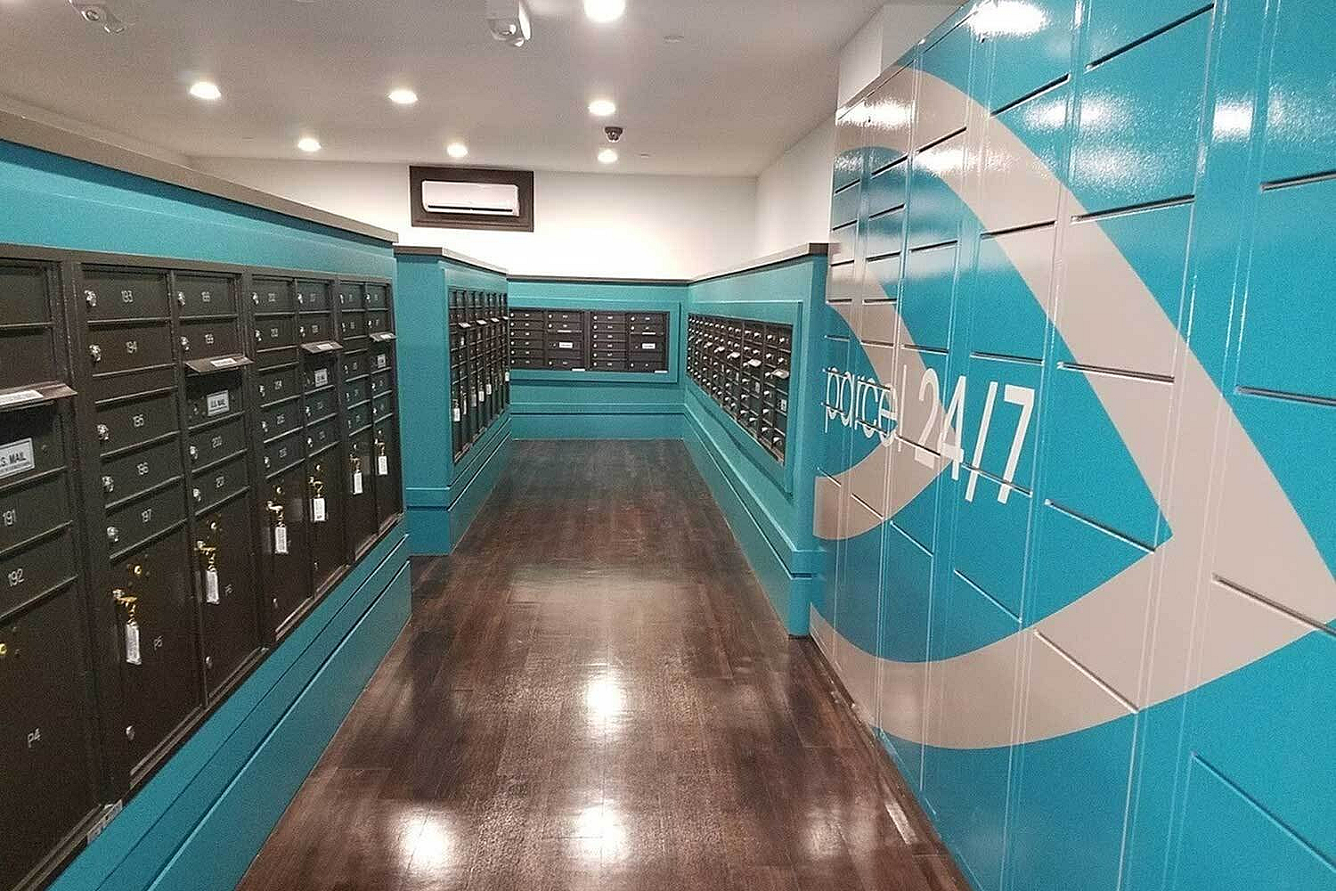 Modern mailroom with sleek black mailboxes and vibrant teal walls featuring 24/7 access signage.