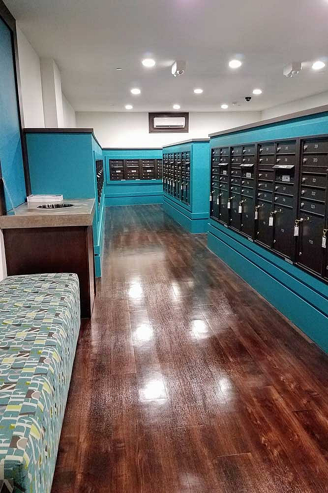 Modern mailroom with sleek blue accents, polished wooden floors, and ample mailbox storage for residents' convenience.