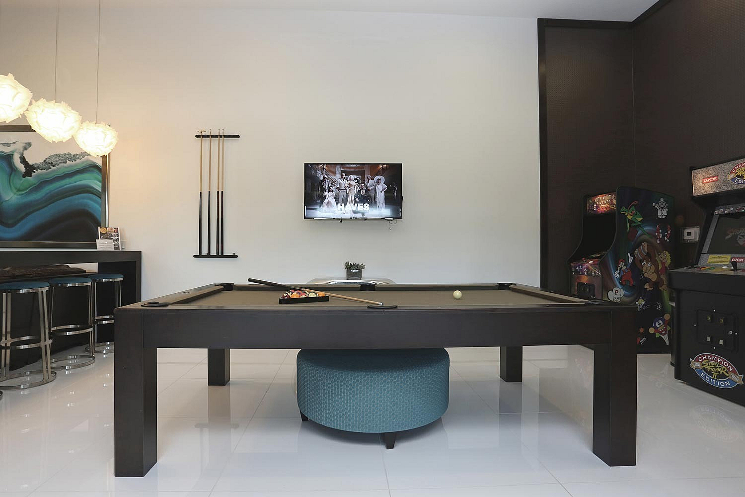 Chic entertainment room with a sleek pool table, retro arcade games, and stylish bar seating under modern lighting.