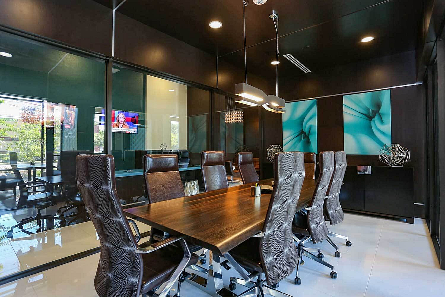 Modern conference room featuring sleek leather chairs, a polished wooden table, and vibrant abstract art. Glass walls and contemporary lighting enhance the professional atmosphere.