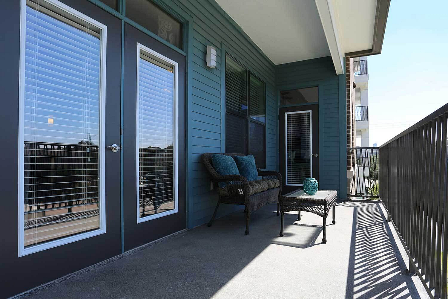 Charming apartment balcony with a cozy wicker settee, stylish coffee table, and inviting panoramic view.