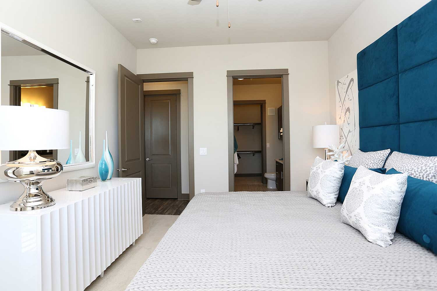 Elegant bedroom with plush teal headboard, stylish decor, and a well-lit inviting atmosphere.