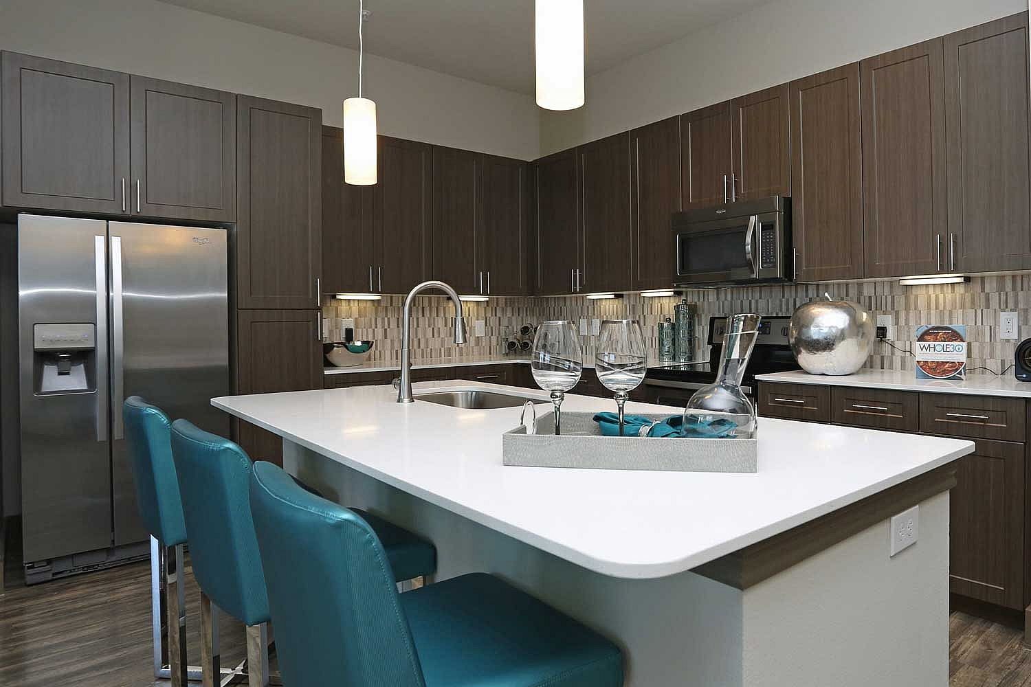 Modern kitchen with sleek dark cabinetry, elegant island with glossy countertop, and vibrant teal bar stools, perfect for entertaining.