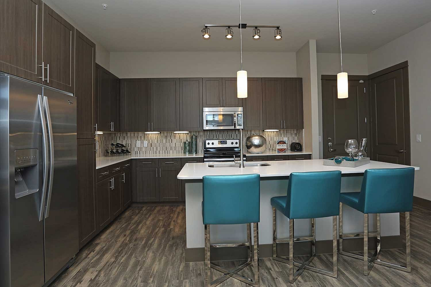Modern kitchen with sleek cabinetry, stainless steel appliances, and a stylish island with turquoise bar stools.