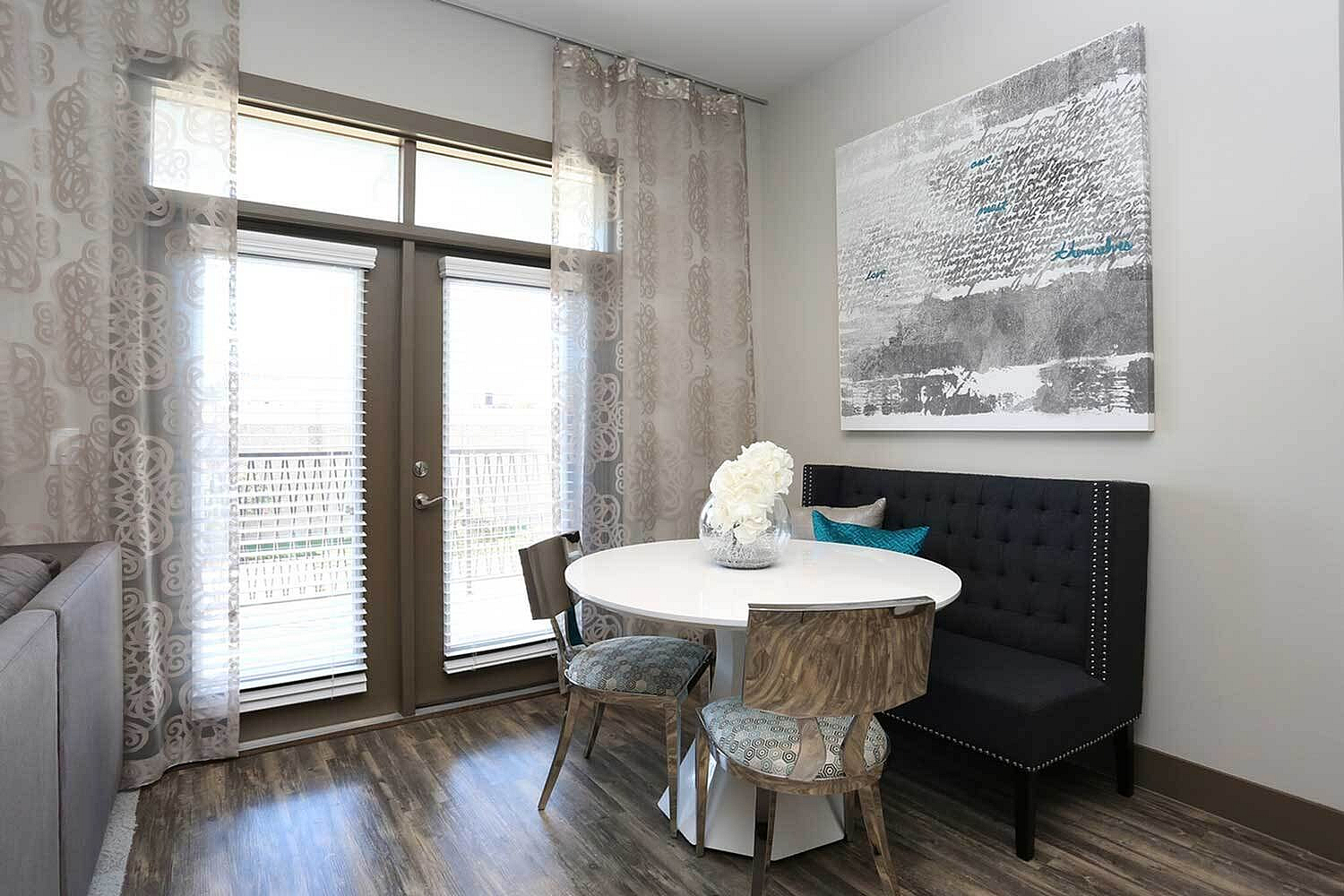 Elegant dining area featuring a round table with chic chairs, plush bench seating, and modern artwork, set against large windows with patterned curtains.
