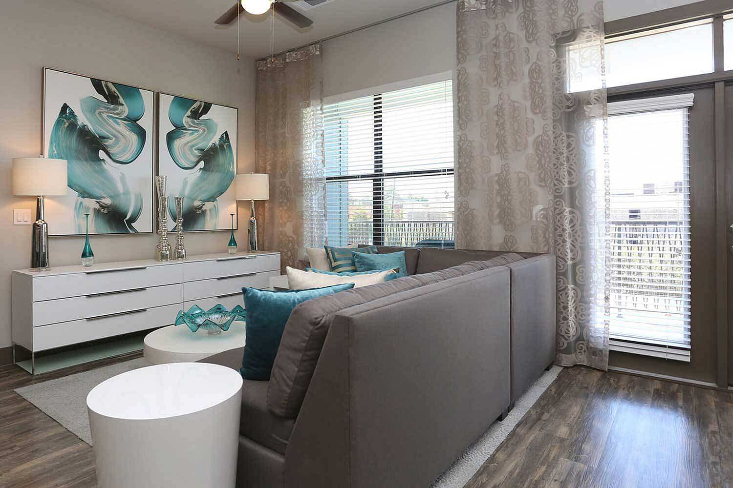 Modern living room with elegant decor, featuring a cozy gray couch, vibrant teal accents, and abstract art on the walls.