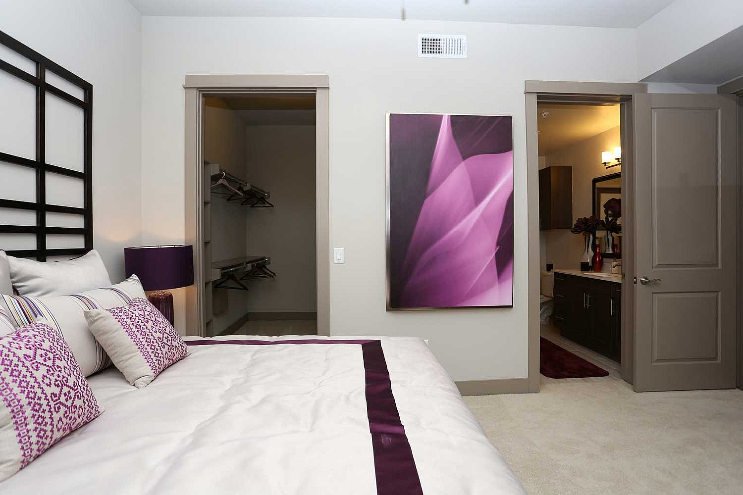 Elegant bedroom with a plush bed adorned with purple accents, spacious walk-in closet, and a modern en-suite bathroom featuring contemporary decor.