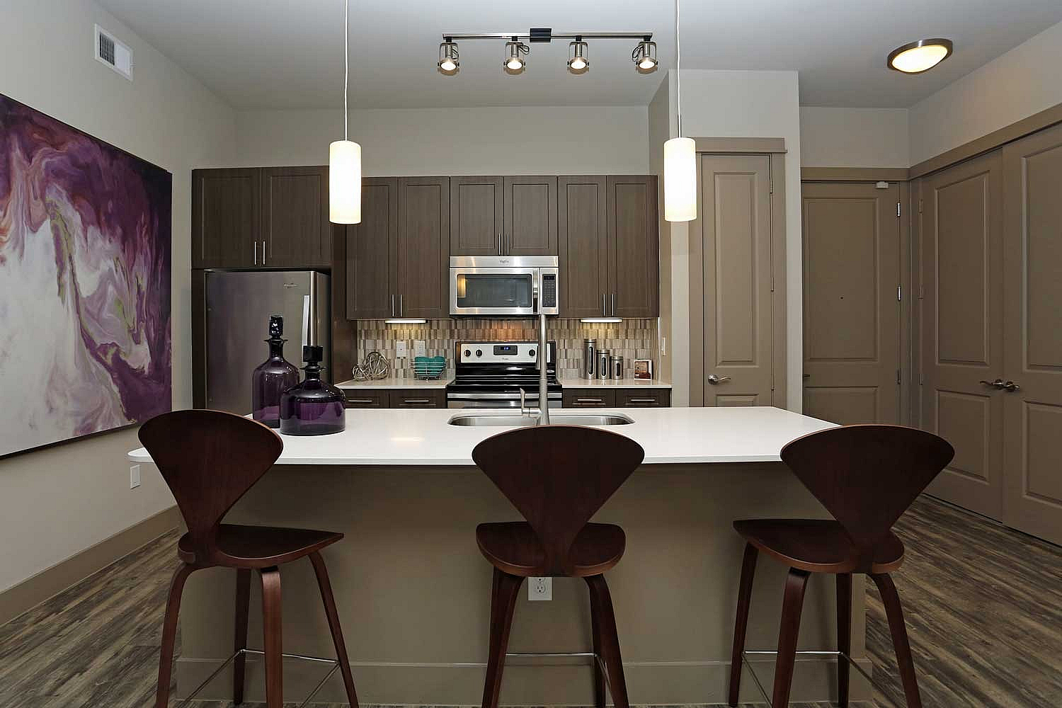 Modern kitchen with sleek dark wood cabinets, stainless steel appliances, and elegant pendant lighting over a stylish island with contemporary barstools.