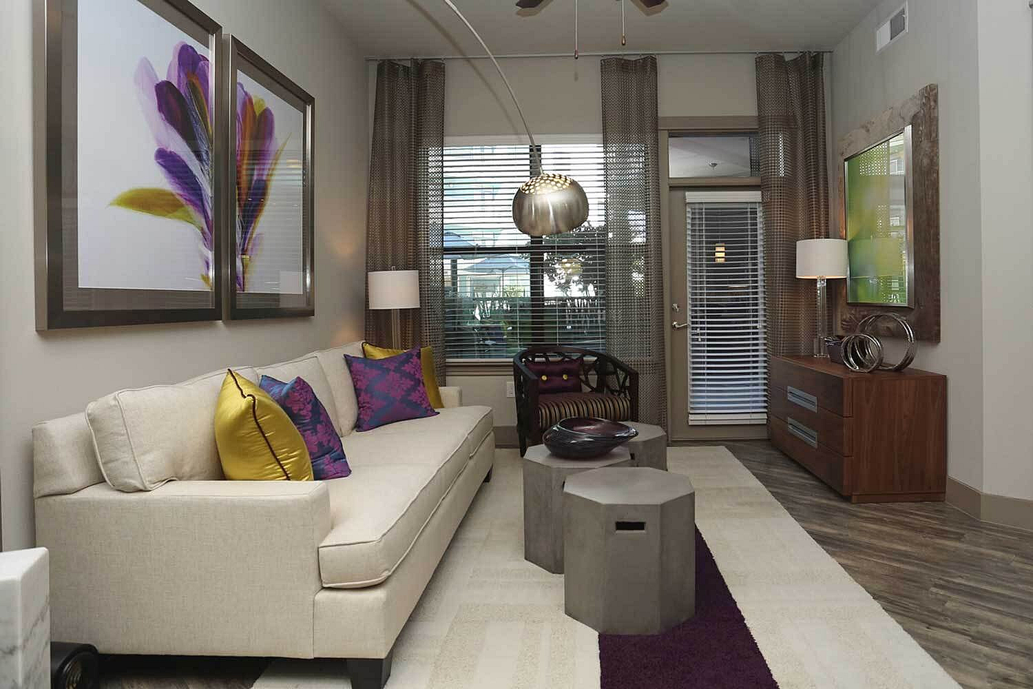 Chic living room with elegant decor, featuring a plush sofa with vibrant cushions, modern art, stylish lighting, and a view of a cozy balcony.