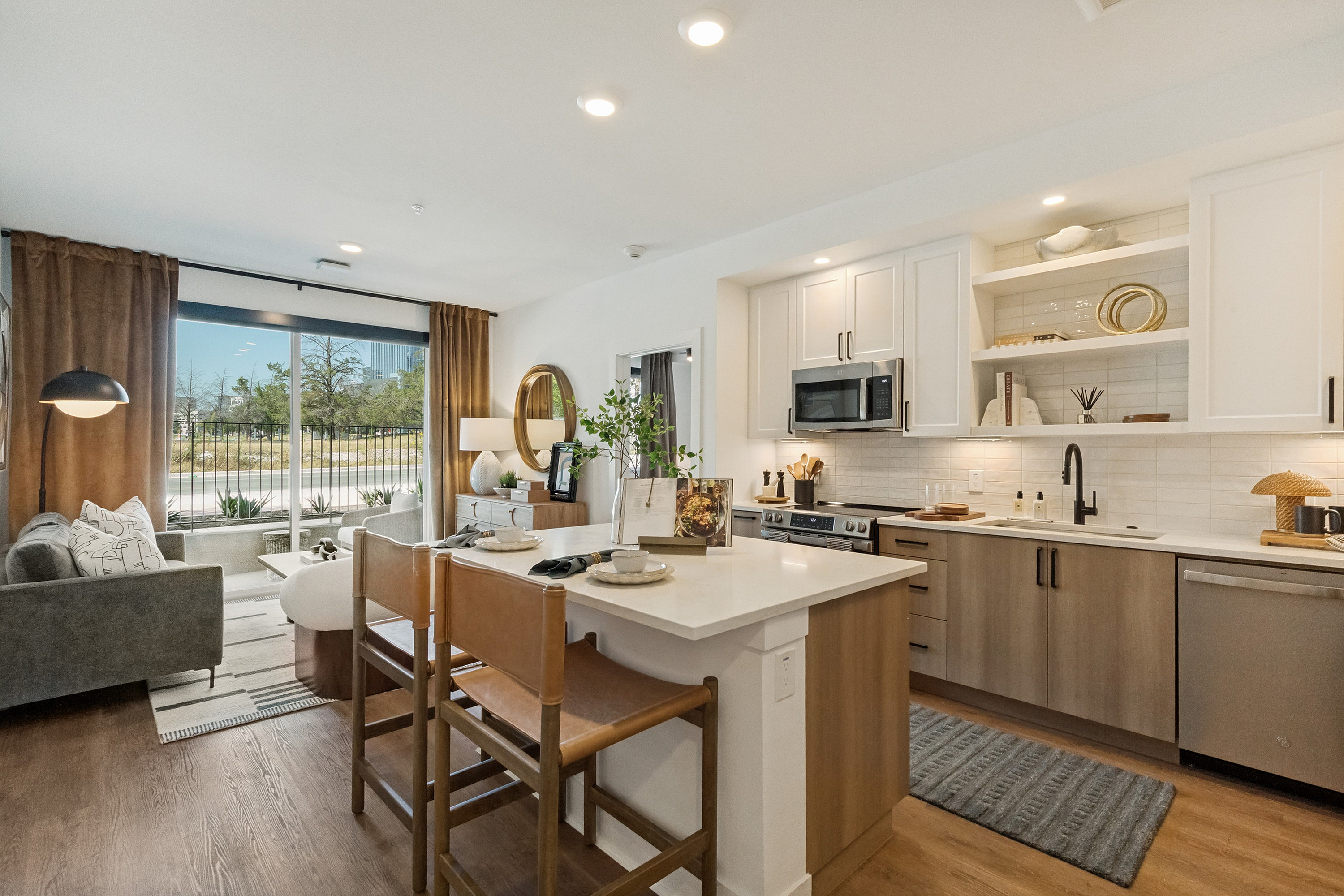 Contemporary apartment interior showcasing a sleek kitchen and cozy living area with large windows and stylish decor.