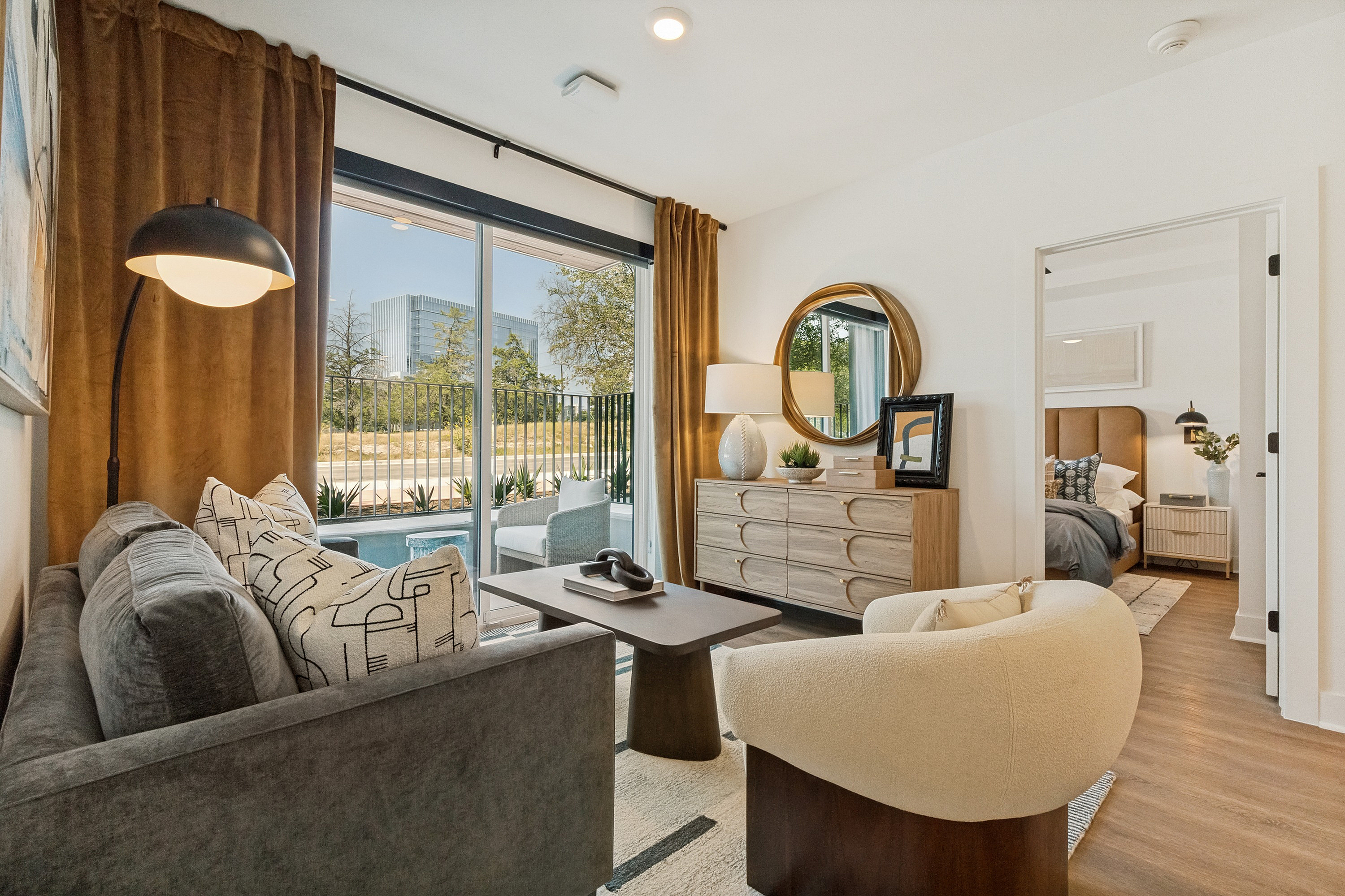 Bright and inviting living area with modern decor, featuring a plush sofa, elegant armchair, and a stunning view through large glass doors leading to a private outdoor oasis.