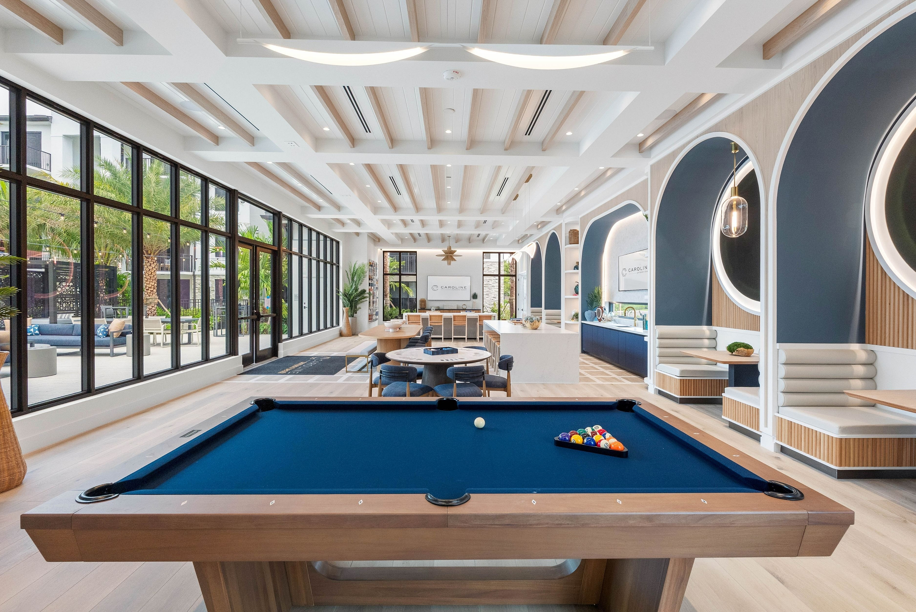 Luxurious recreational area featuring a sleek pool table, cozy seating, and expansive windows overlooking lush greenery.