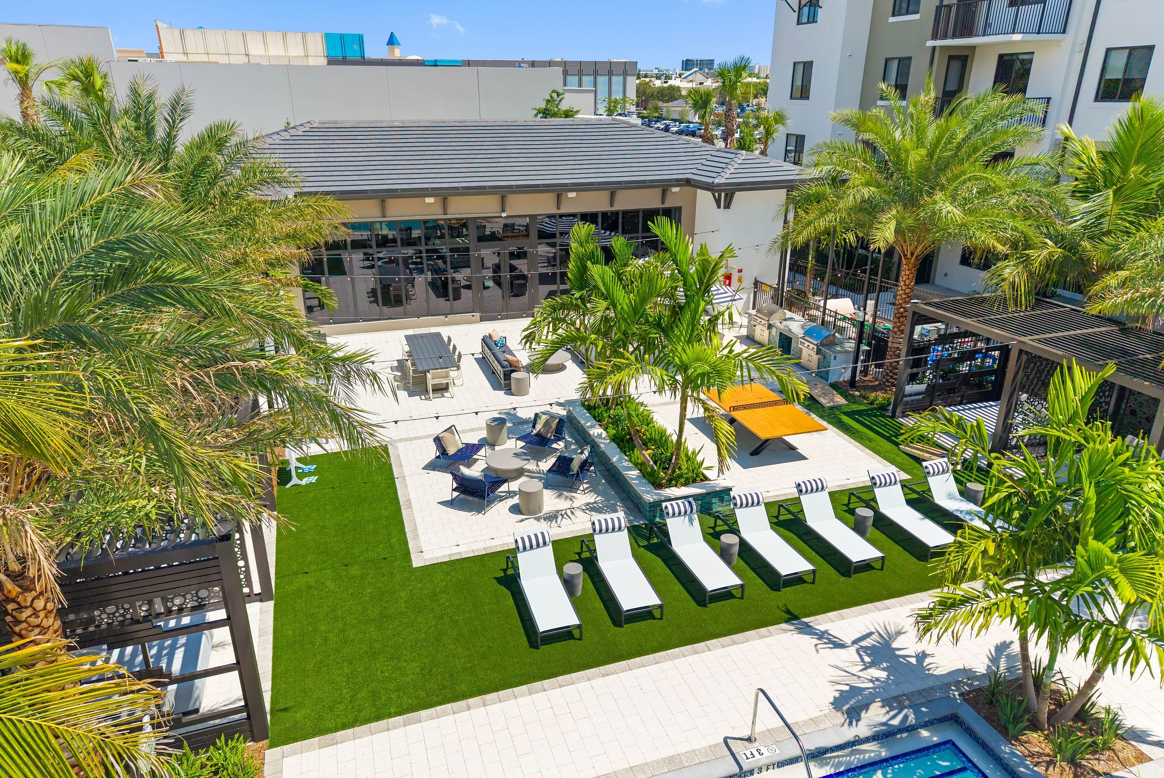 Luxurious outdoor lounge area with palm trees, sun loungers, and a barbecue setup, perfect for relaxation and entertaining.