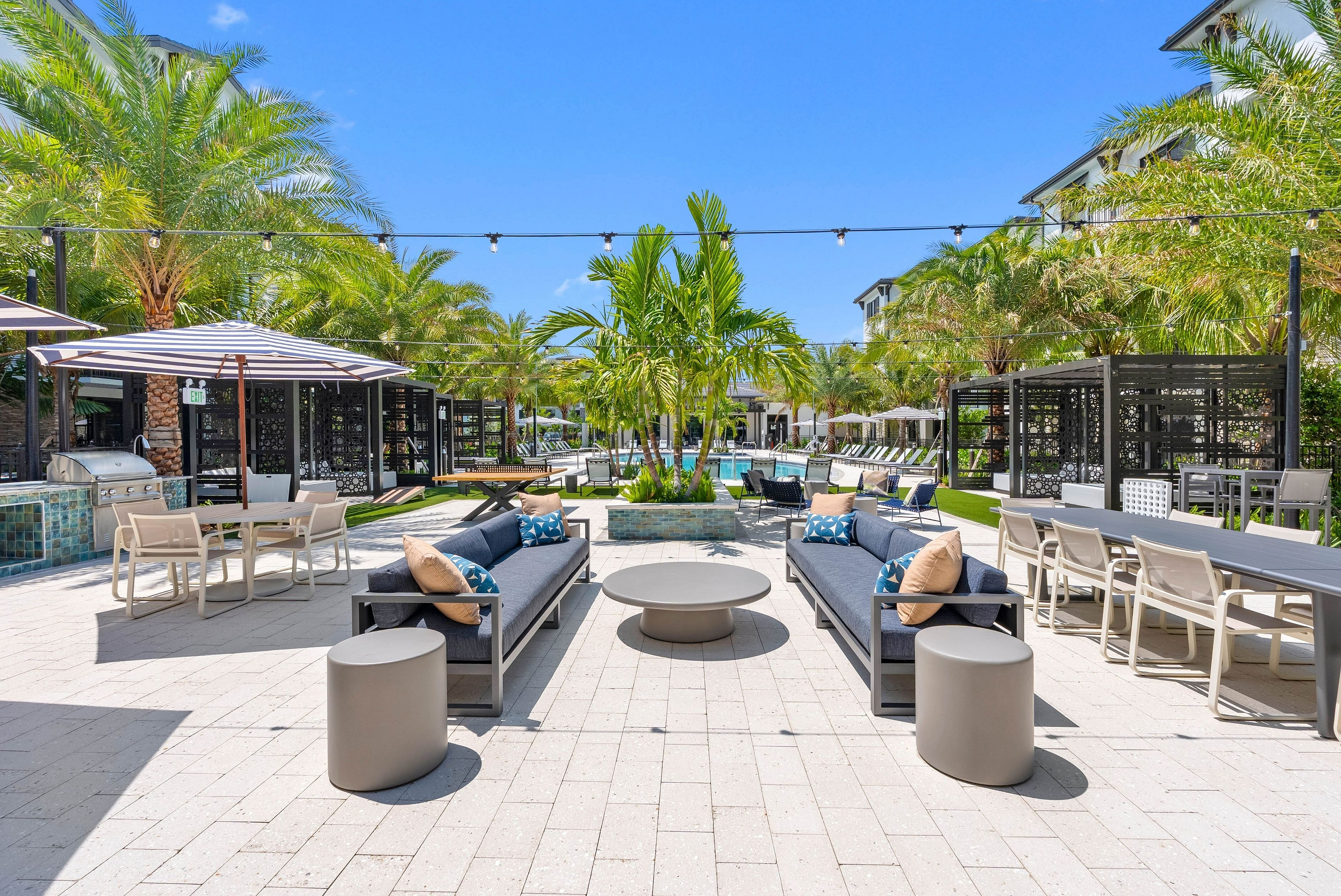 Luxury outdoor lounge with stylish seating, vibrant palm trees, and a sparkling swimming pool under a clear blue sky.