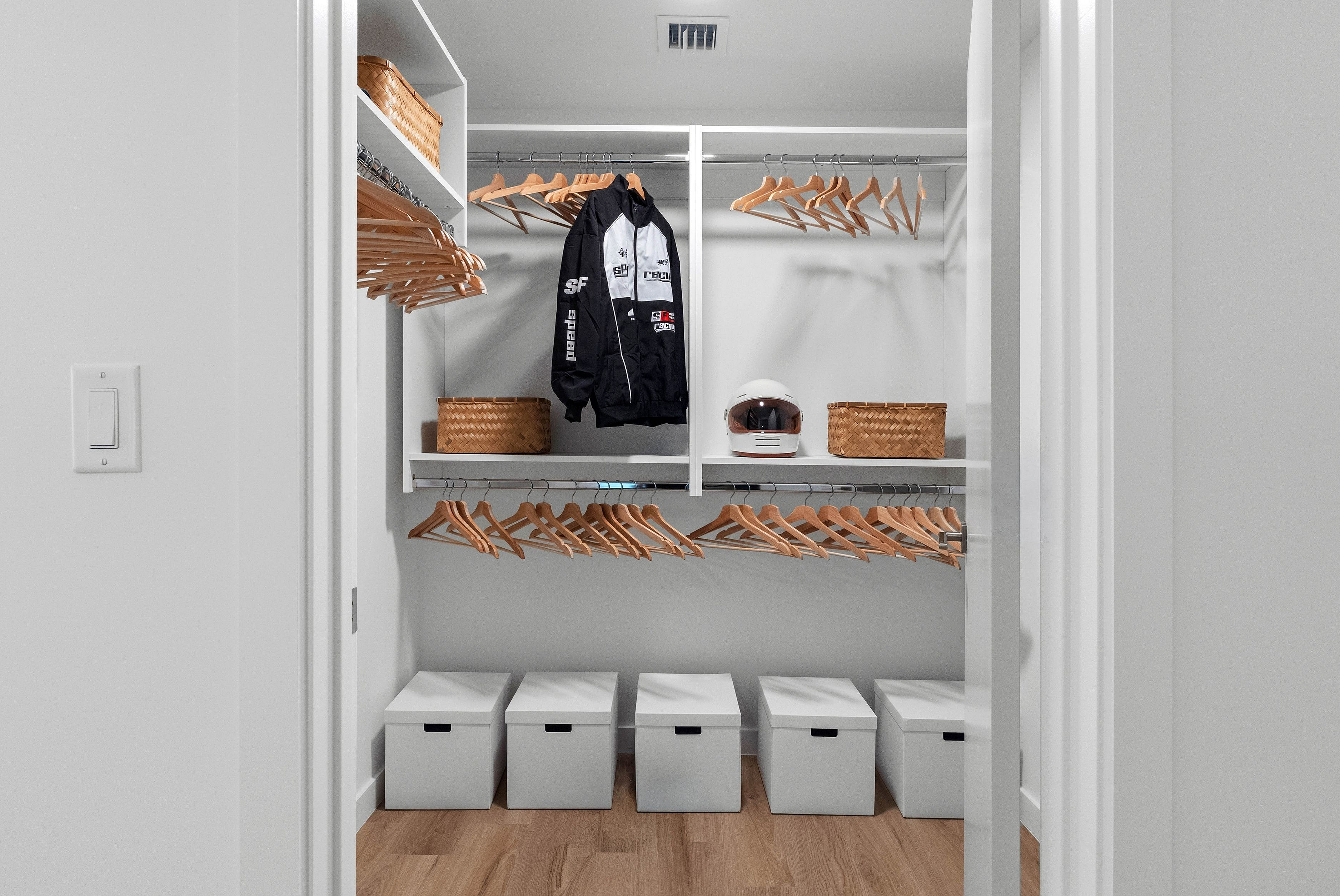 Modern walk-in closet with ample storage, featuring sleek wooden hangers, woven baskets, and stylish white storage boxes.