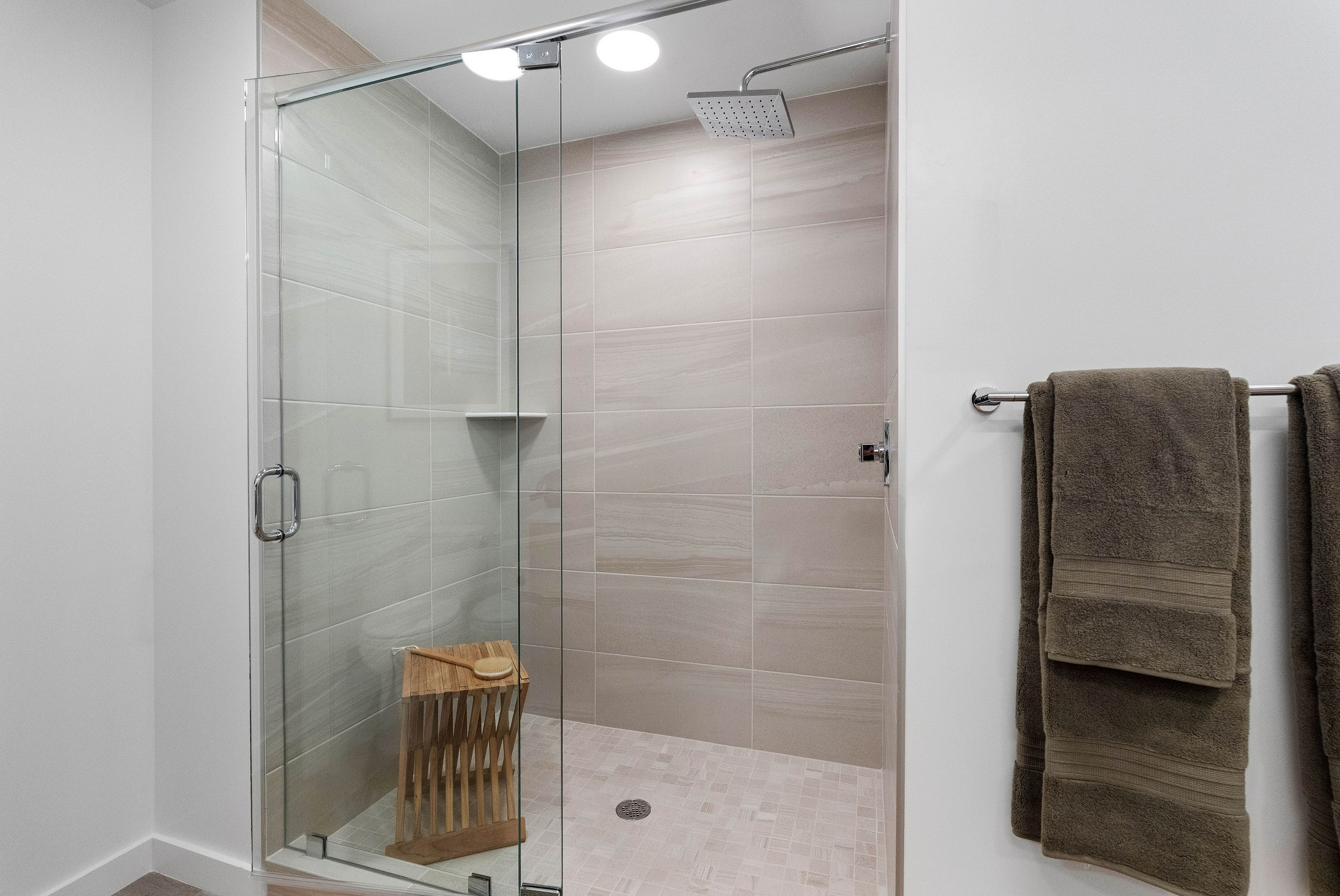 Luxurious modern shower with glass doors and elegant tiled walls, featuring sleek fixtures and plush towels for a spa-like experience.