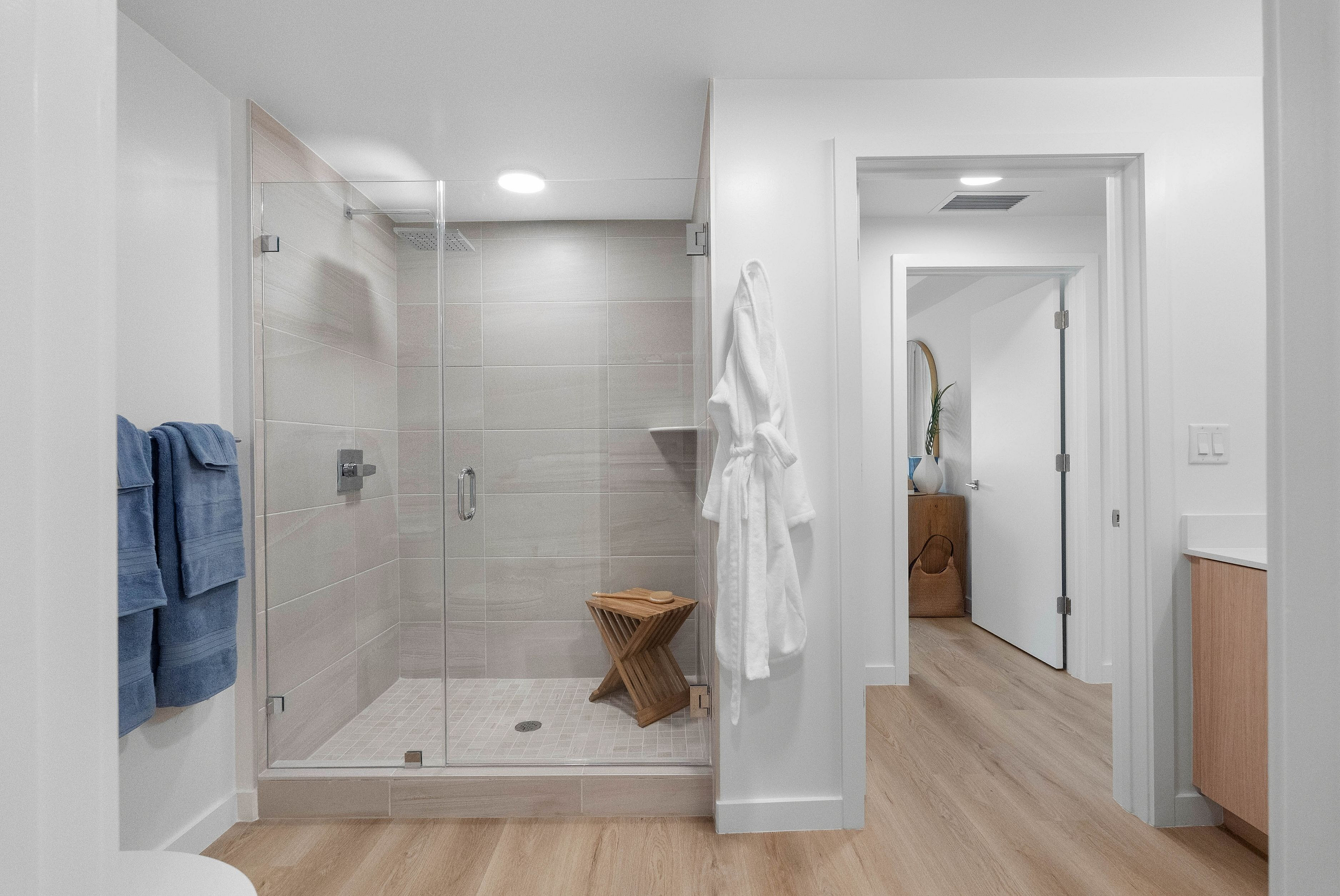 Elegant modern bathroom with a glass-enclosed shower, wooden stool, and soft lighting for a relaxing atmosphere.