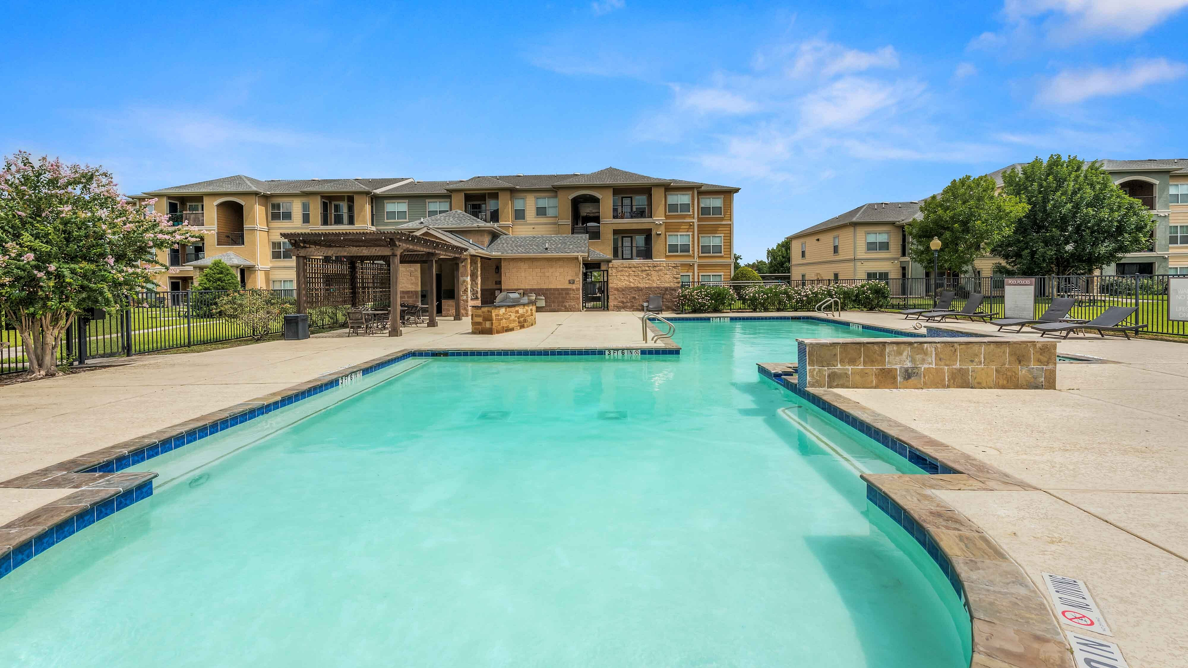 Apartment swimming pool surrounded by lounge seating and landscaping