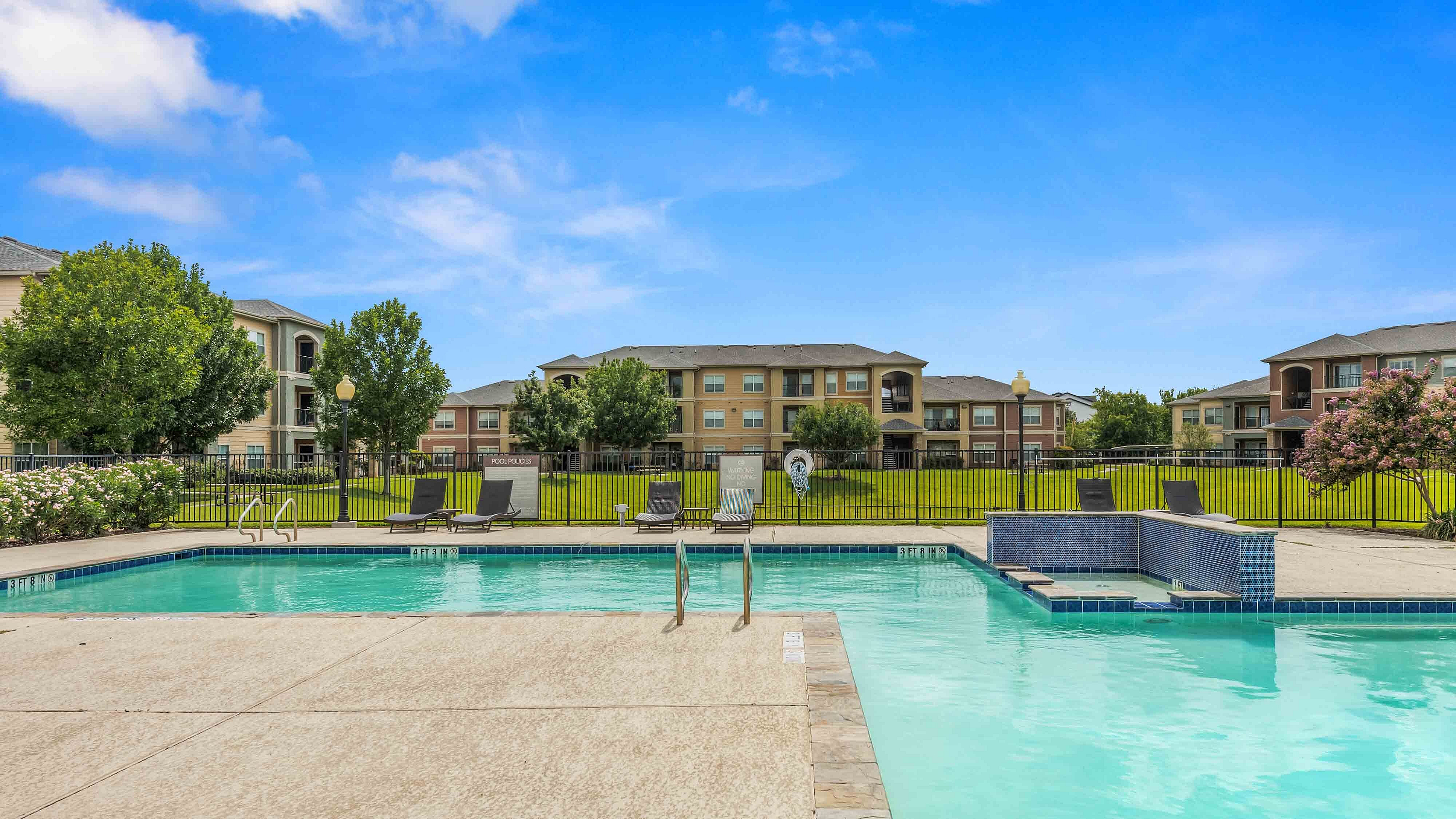 Swimming pool surrounded by apartment buildings, green space, and landscaping