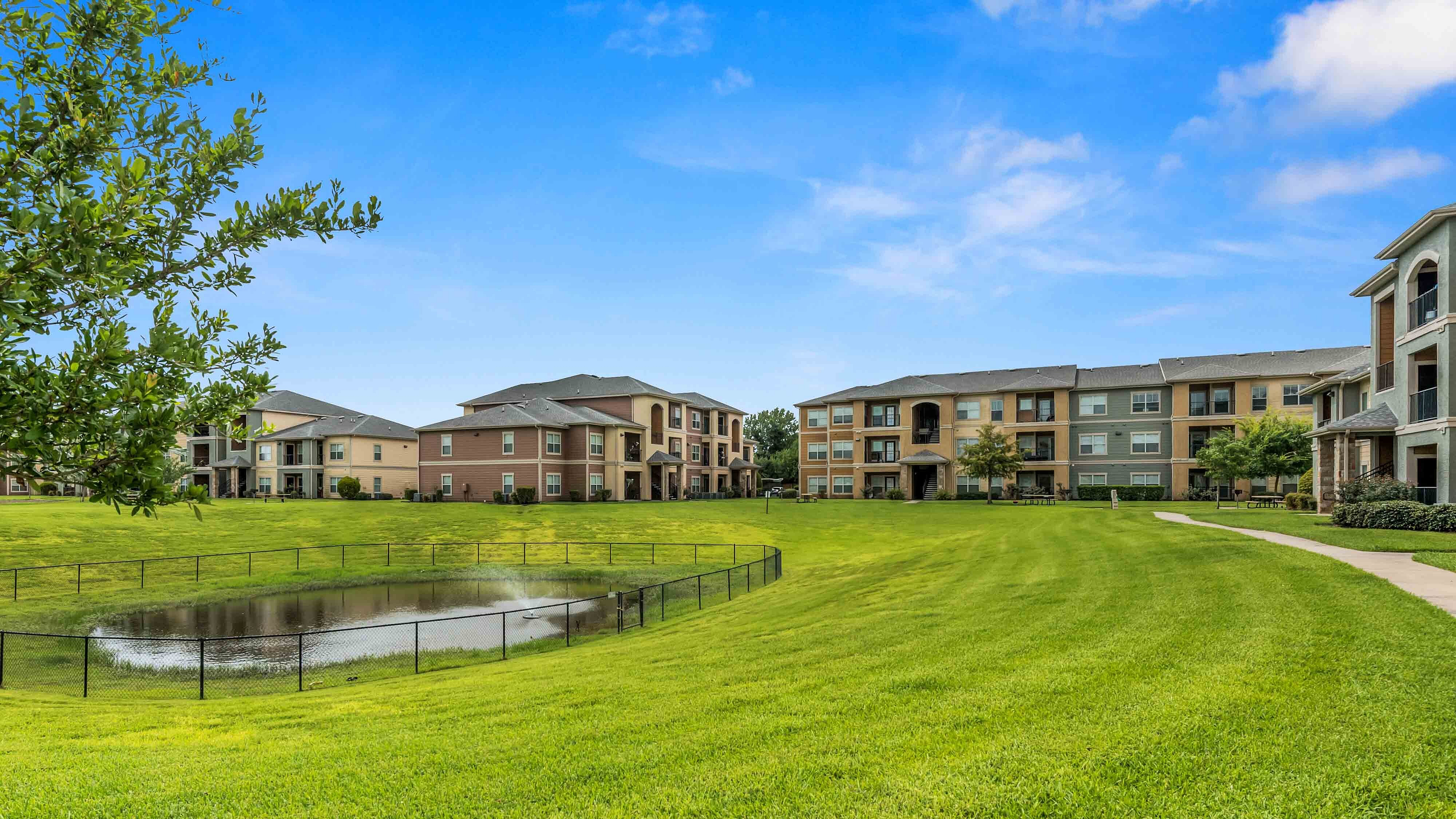 Apartment community green space with walking paths, pond, and residential buildings