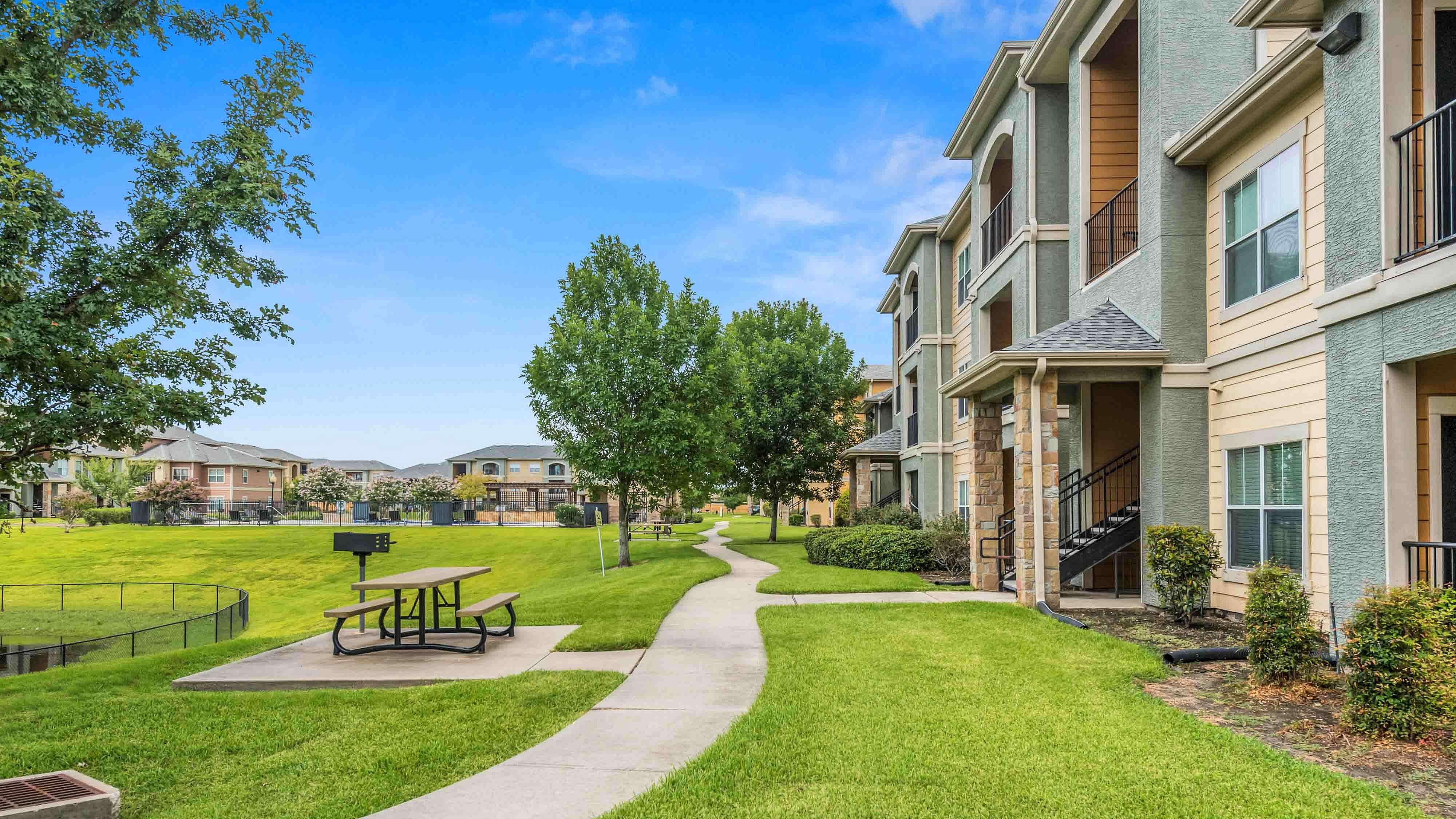 Landscaped walking path beside apartment buildings with picnic area and green space