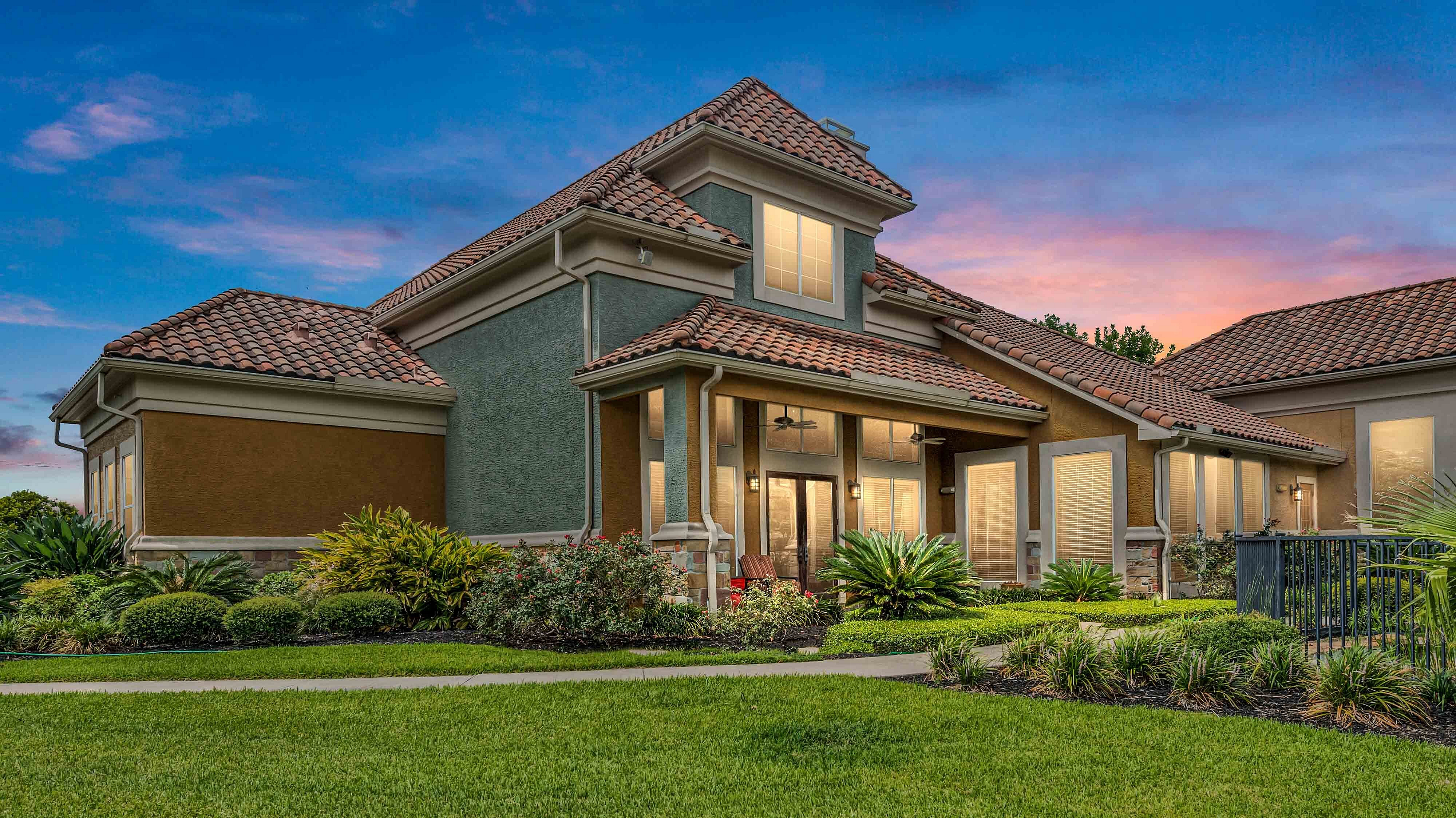 Apartment clubhouse exterior with landscaped grounds at sunset