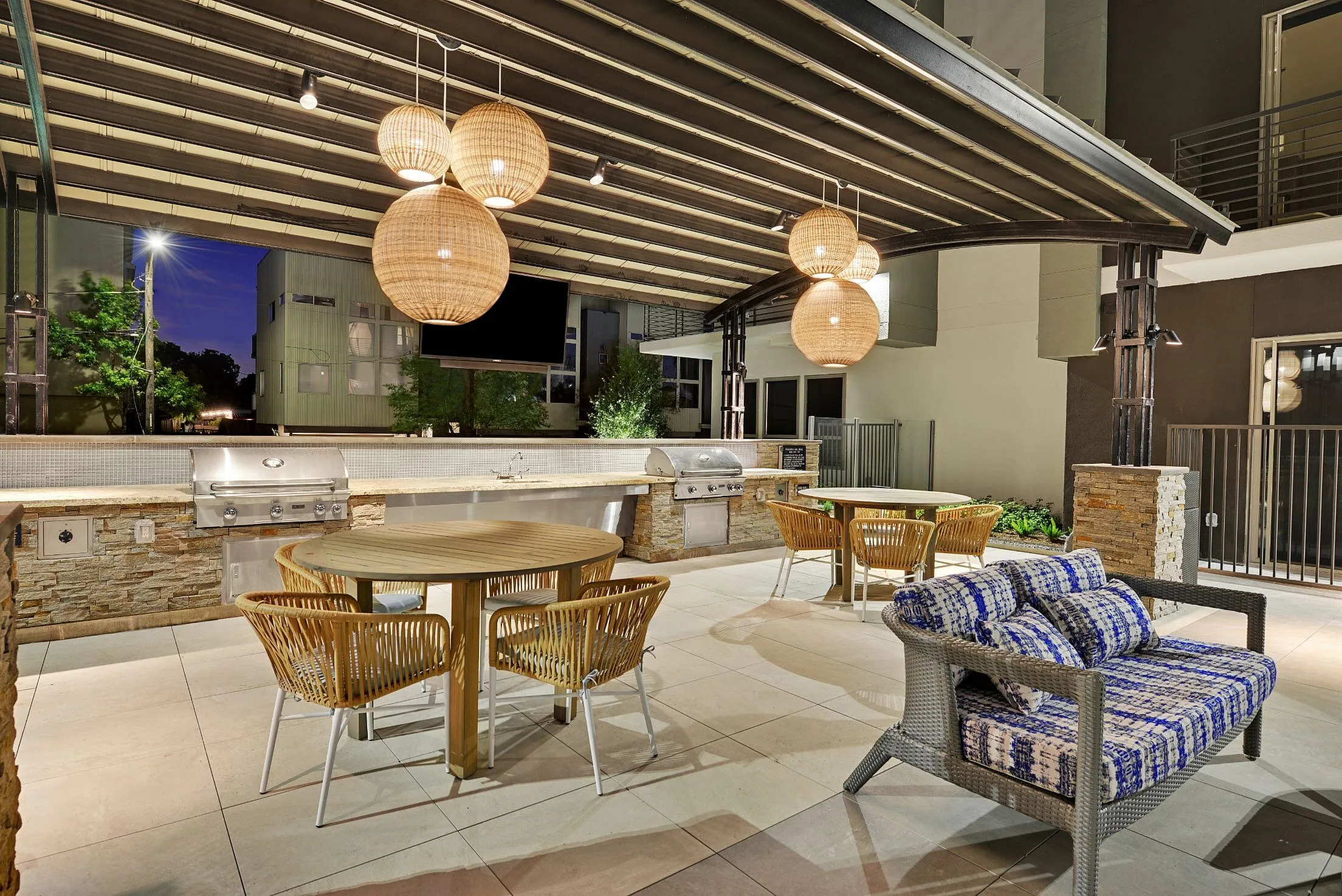 Outdoor kitchen with grills, pendant lights and patio dining under pergola