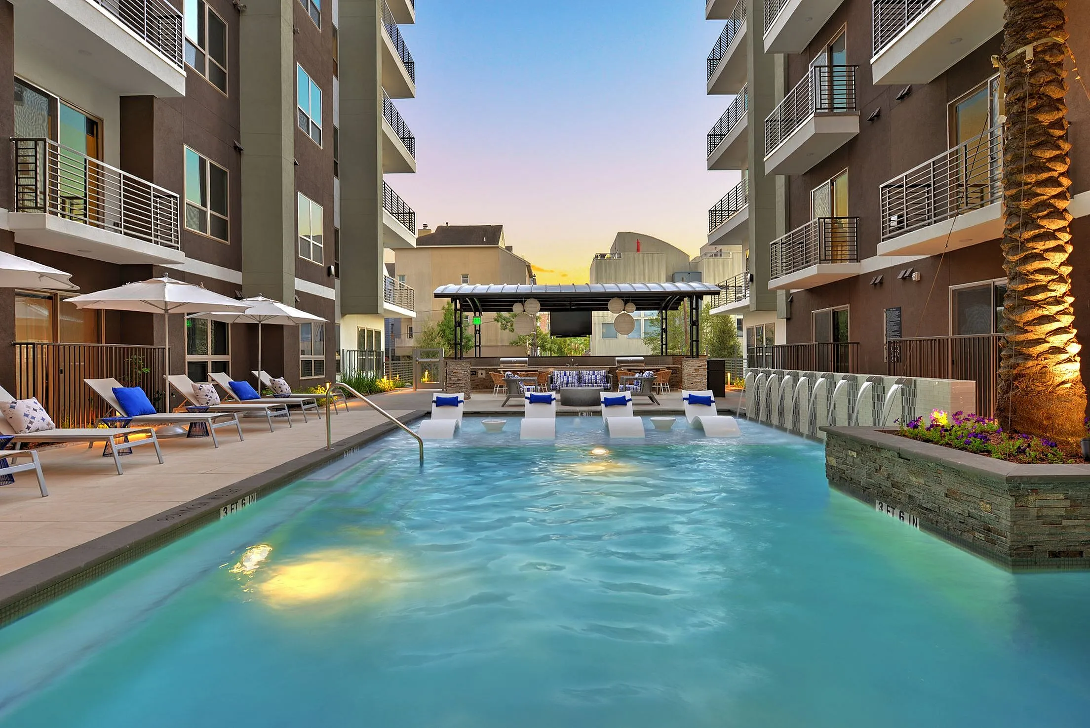 Pool courtyard with lounge chairs, umbrellas and mid-rise buildings at sunset, Houston, TX